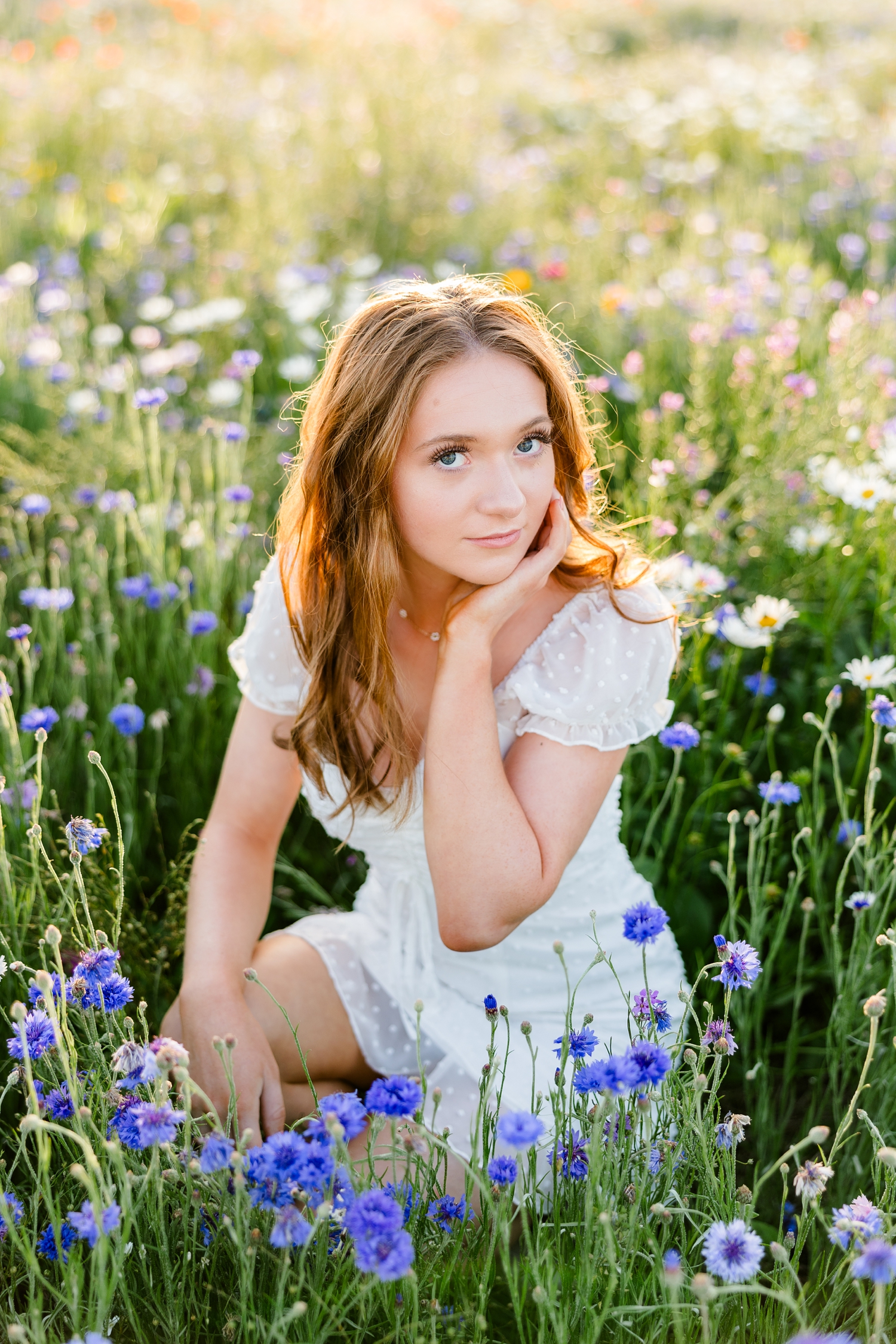 Izzie, wearing a white dress, sits in a field of wildflowers at sunset | CB Studio