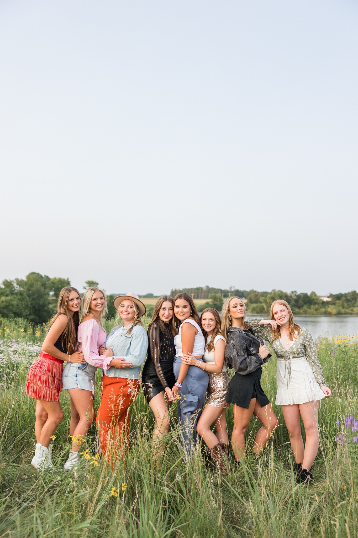 Eight senior spokesmodel rep girls pose in a wildflower field with a lake in a the background dress in Taylor Swift Eras themed outfits | CB Studio