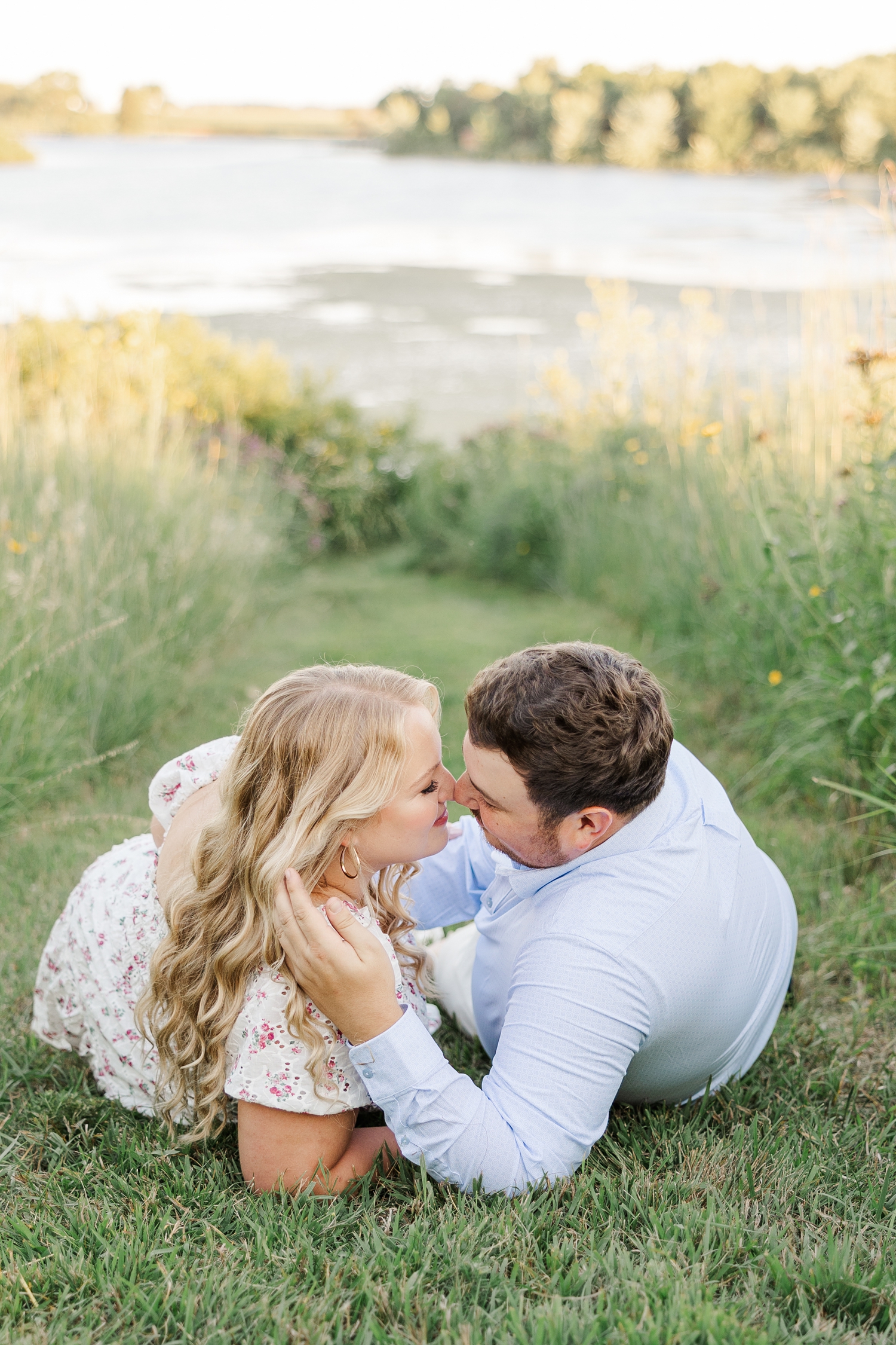 Connor slowly moves Natalie's hair to the side as he goes in for a kiss while they both lay on a grass path at Water's Edge Nature Center | CB Studio