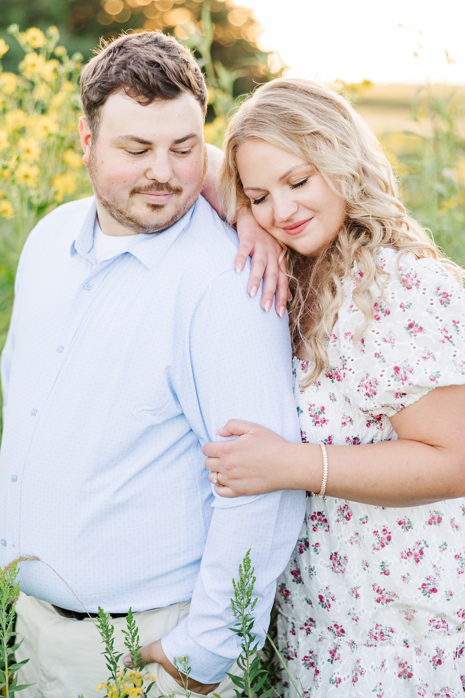 Natalie leans on her fiance's shoulder and looks down as Connor looks back at her, surrounded by yellow cup flowers at Water's Edge Nature Center | CB Studio