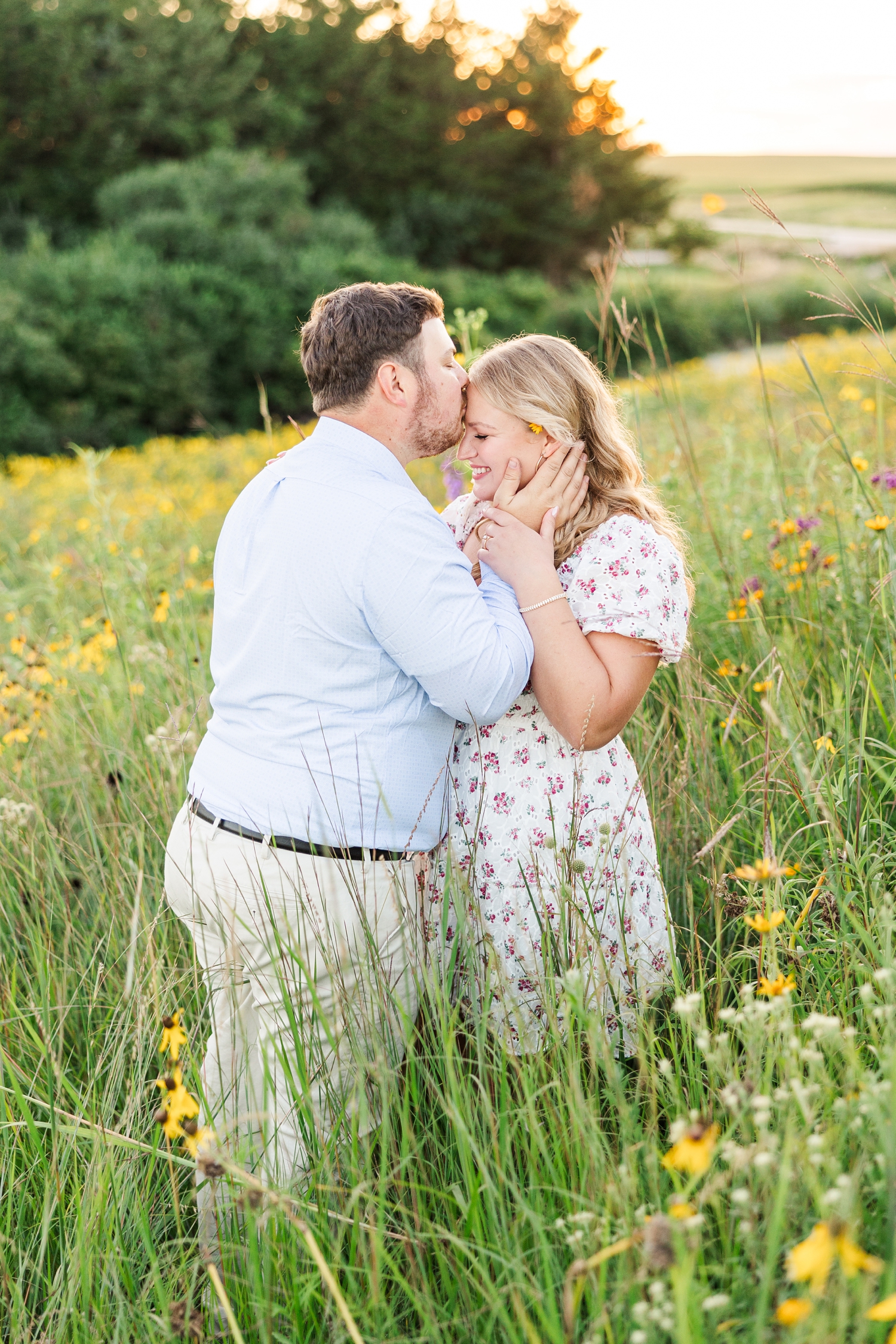 Connor gently holds Natalie's neck and cheek while kissing her on the forehead, surrounded by wildflowers at Water's Edge Nature Center | CB Studio