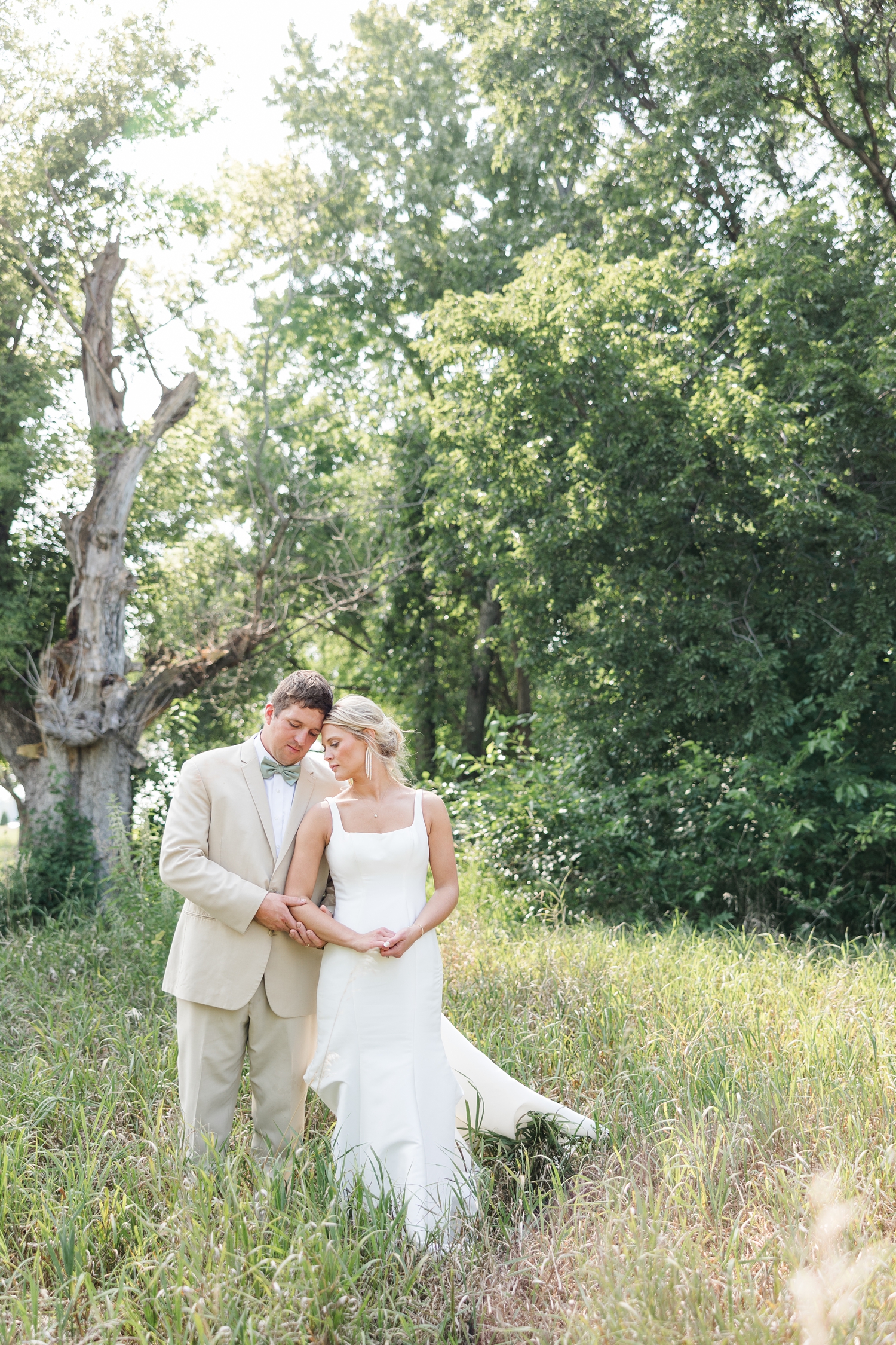 Reed holds his bride's arm as they rest foreheads while standing in a grassy field on their farm in northern Iowa | CB Studio