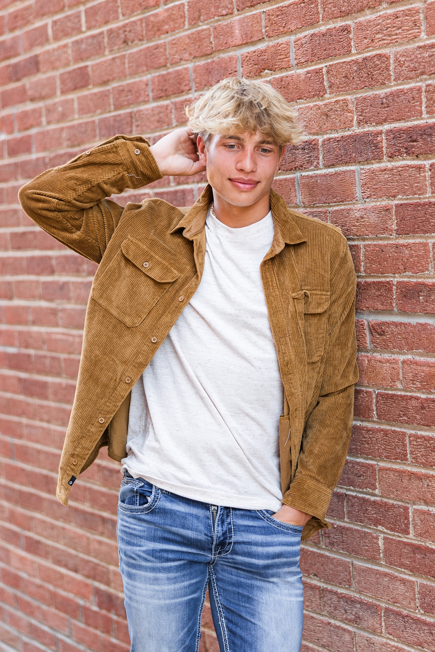 Tyler, while scratching the back of his head and looking down, leans against a brick wall in downtown Algona, IA | CB Studio