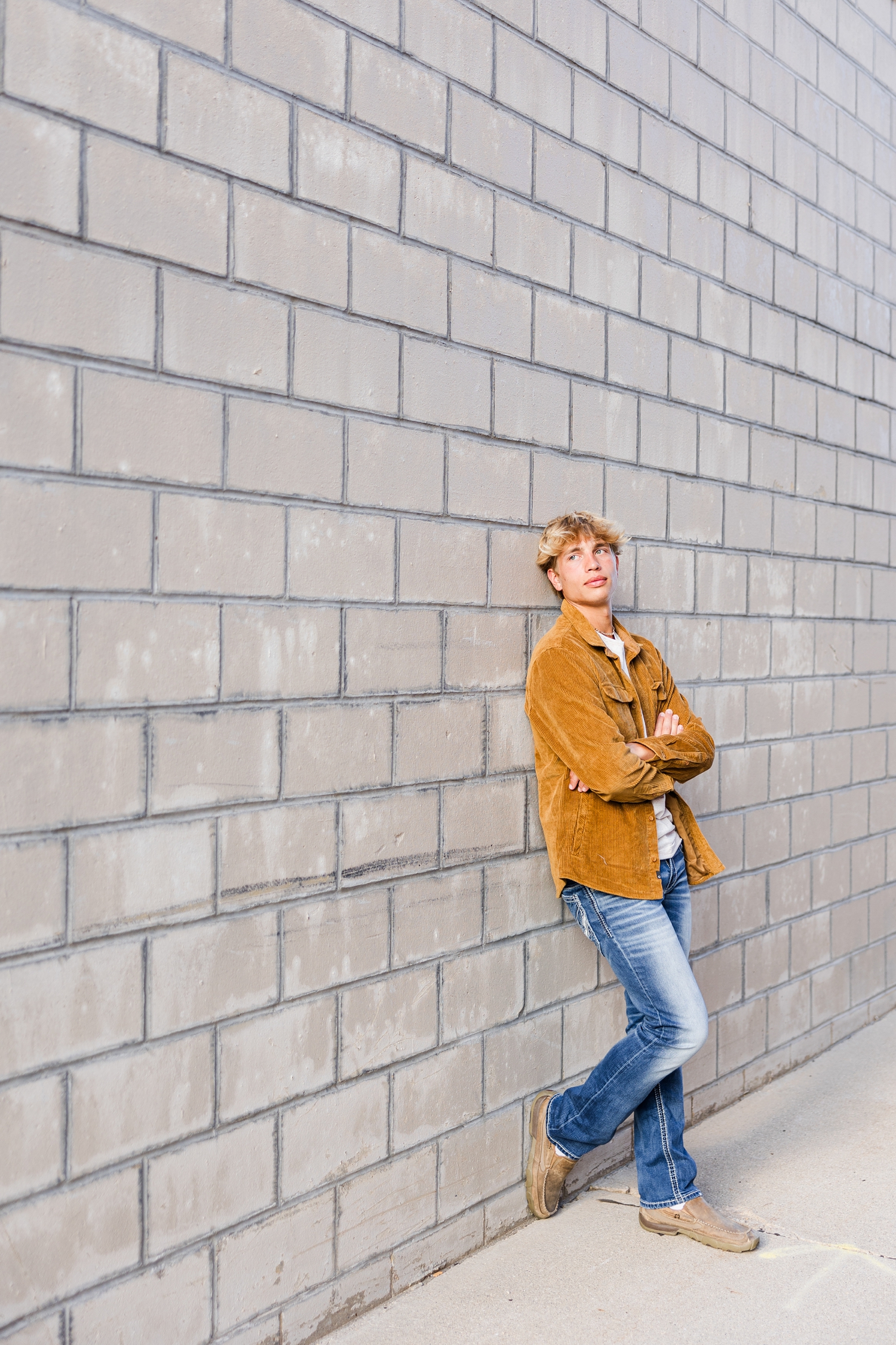 Tyler, with arms crossed, leans against a grey brick wall in downtown Algona, IA | CB Studio