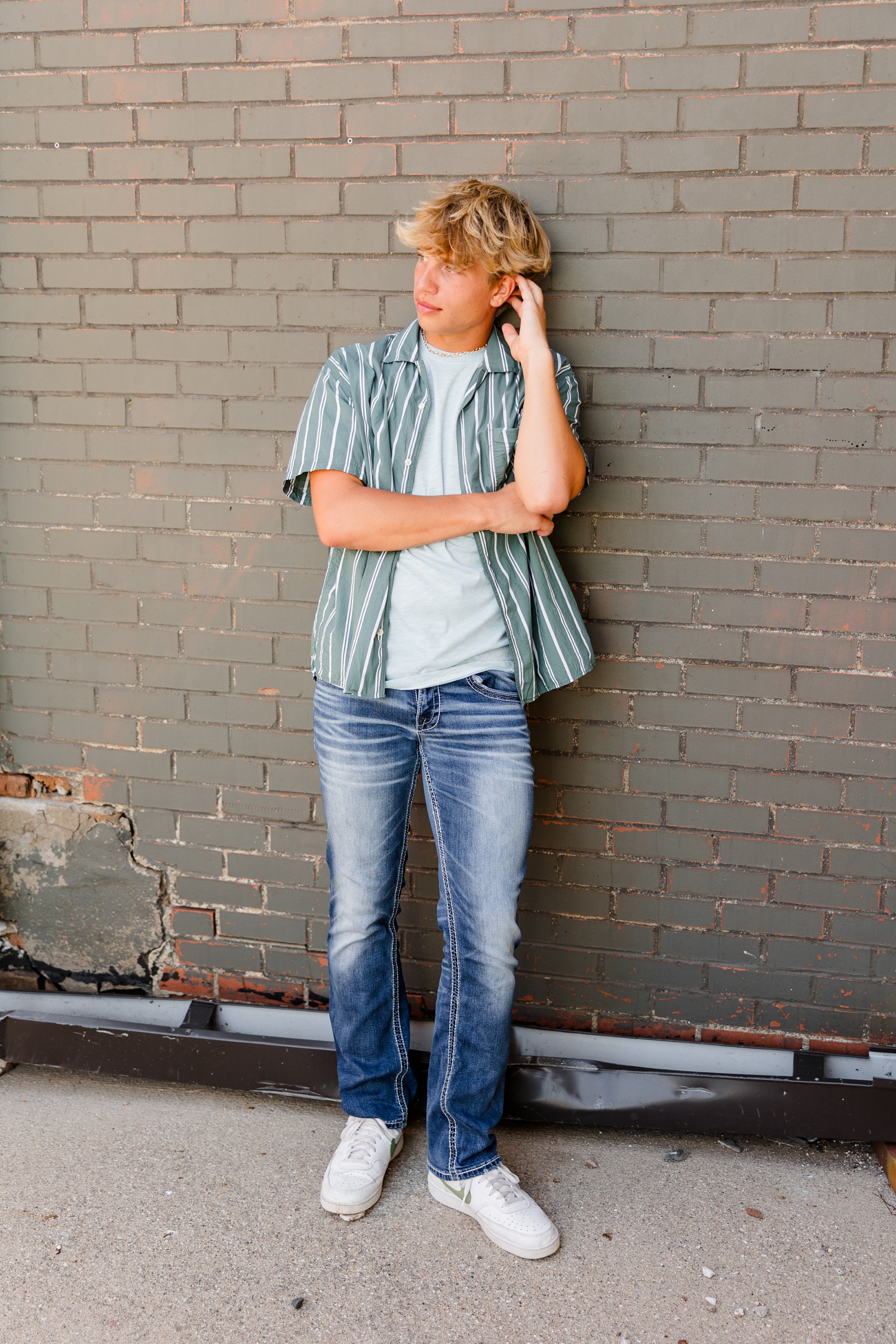 Tyler, while looking to the left, leans against a green brick wall in downtown Algona, IA | CB Studio