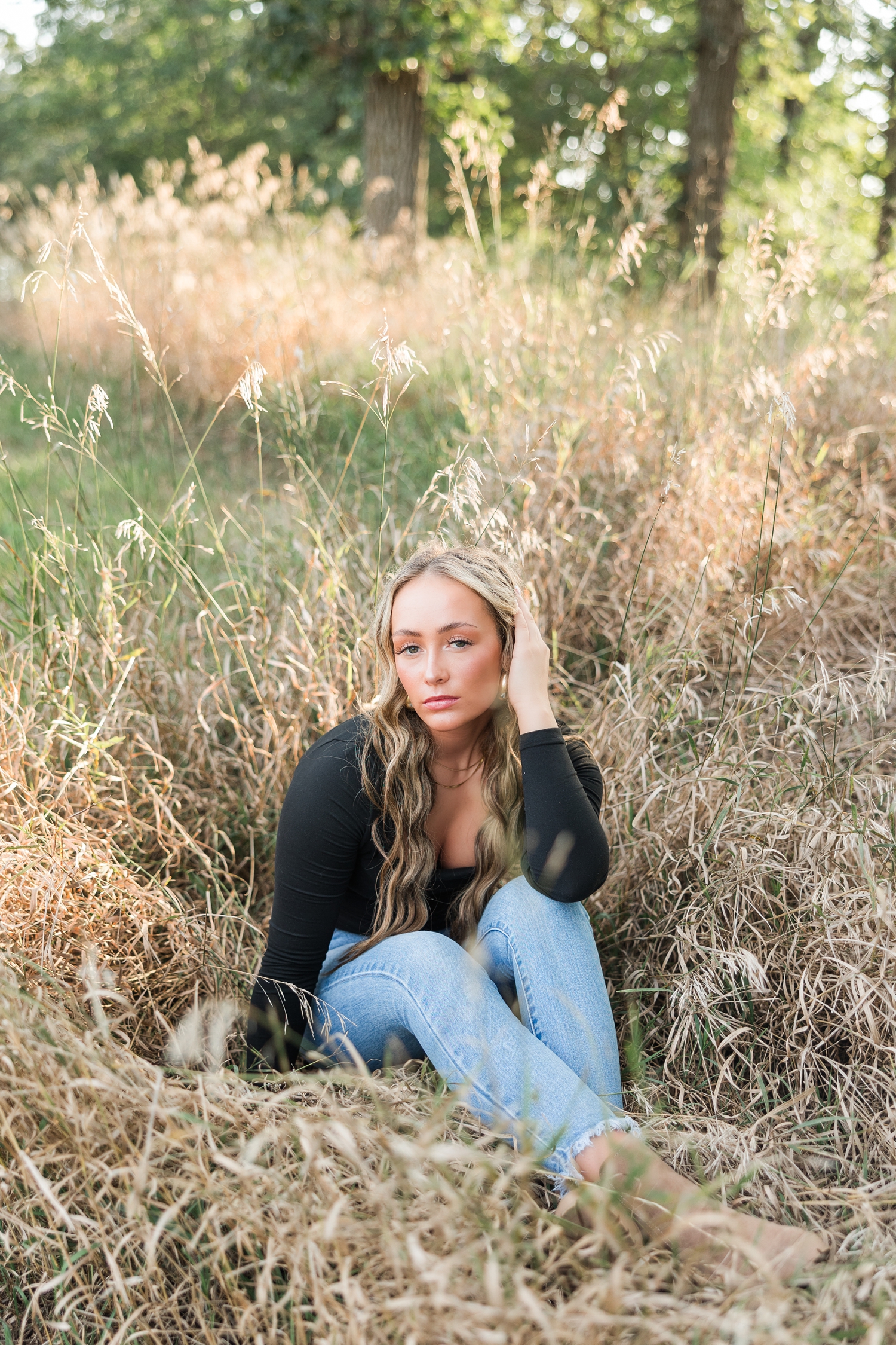 Blaire, wearing jeans and a black long sleeve top, sits in the middle of a grassy field in September | CB Studio