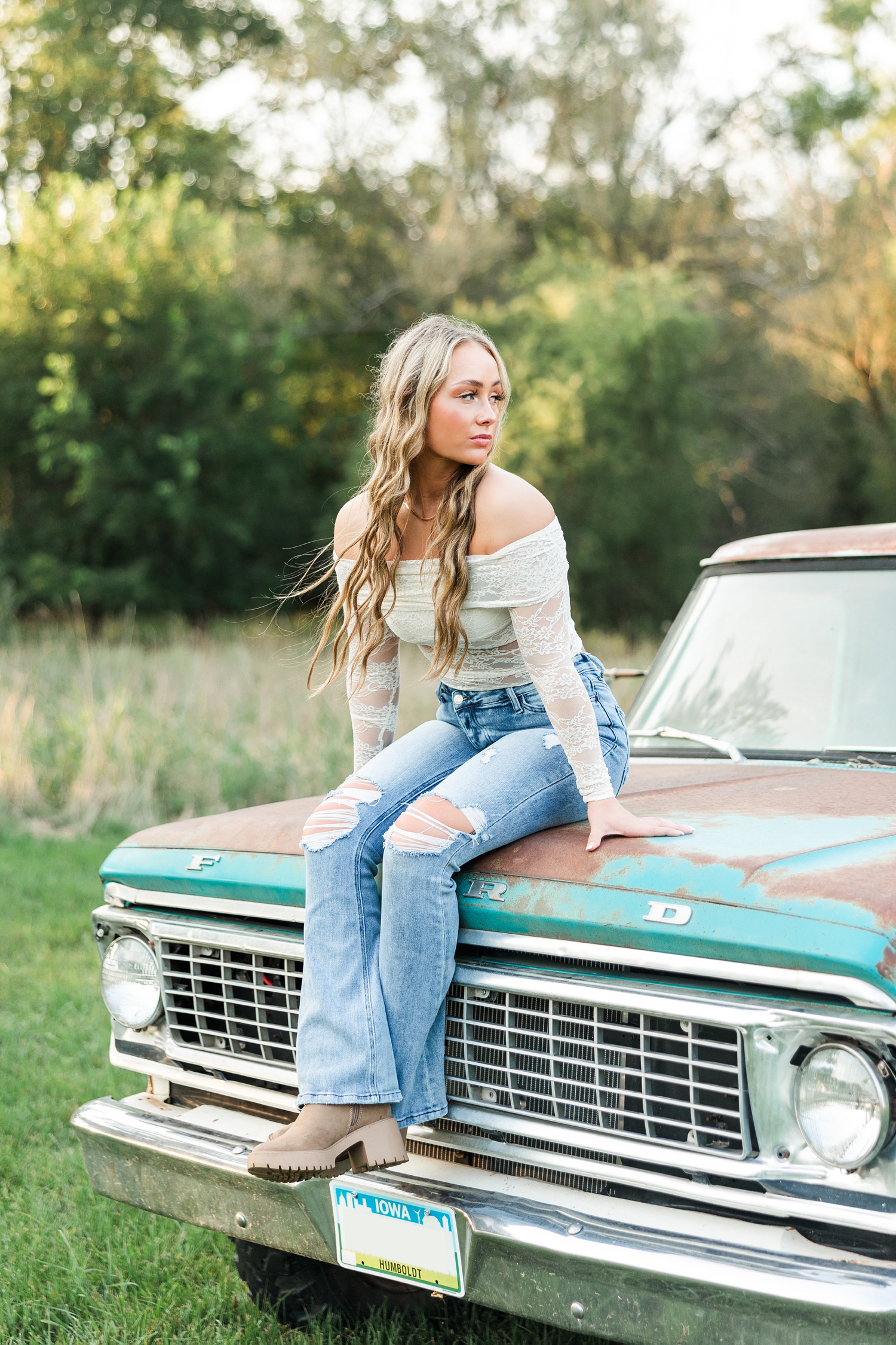 Blaire, wearing white lace off the shoulder long sleeve top, sits on the hood of an old teal and white Ford truck and looks over her left shoulder | CB Studio