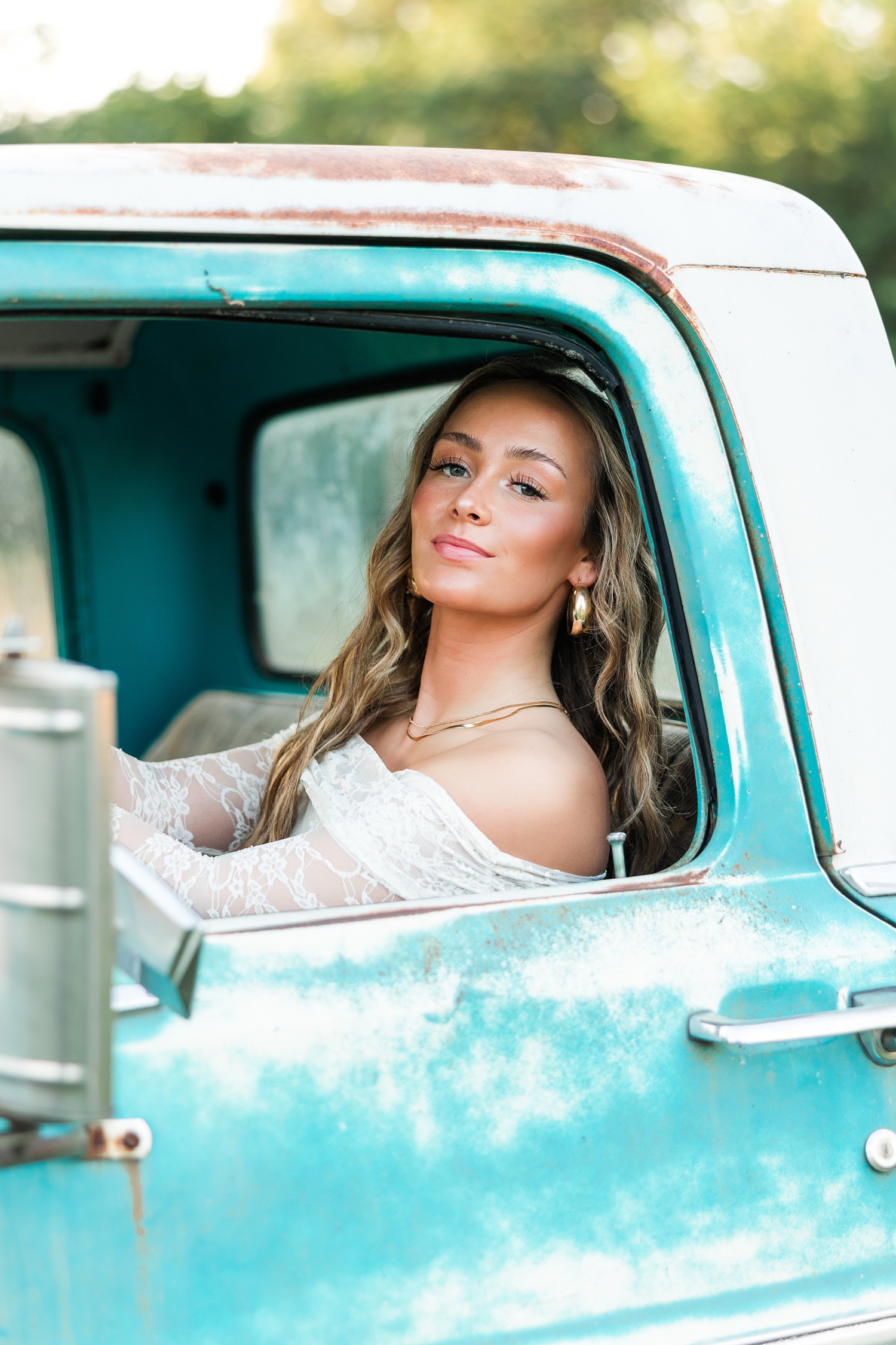 Blaire, wearing white lace off the shoulder long sleeve top, sits in the driver's seat of an old teal and white Ford truck | CB Studio