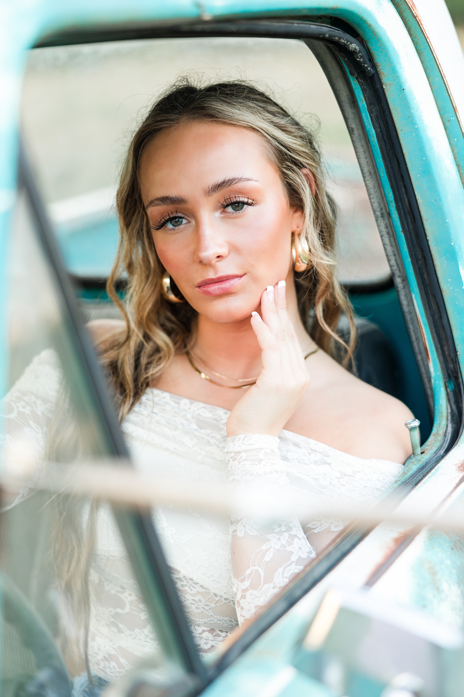 Blaire, wearing white lace off the shoulder long sleeve top, sits in the driver's seat of an old teal and white Ford truck | CB Studio