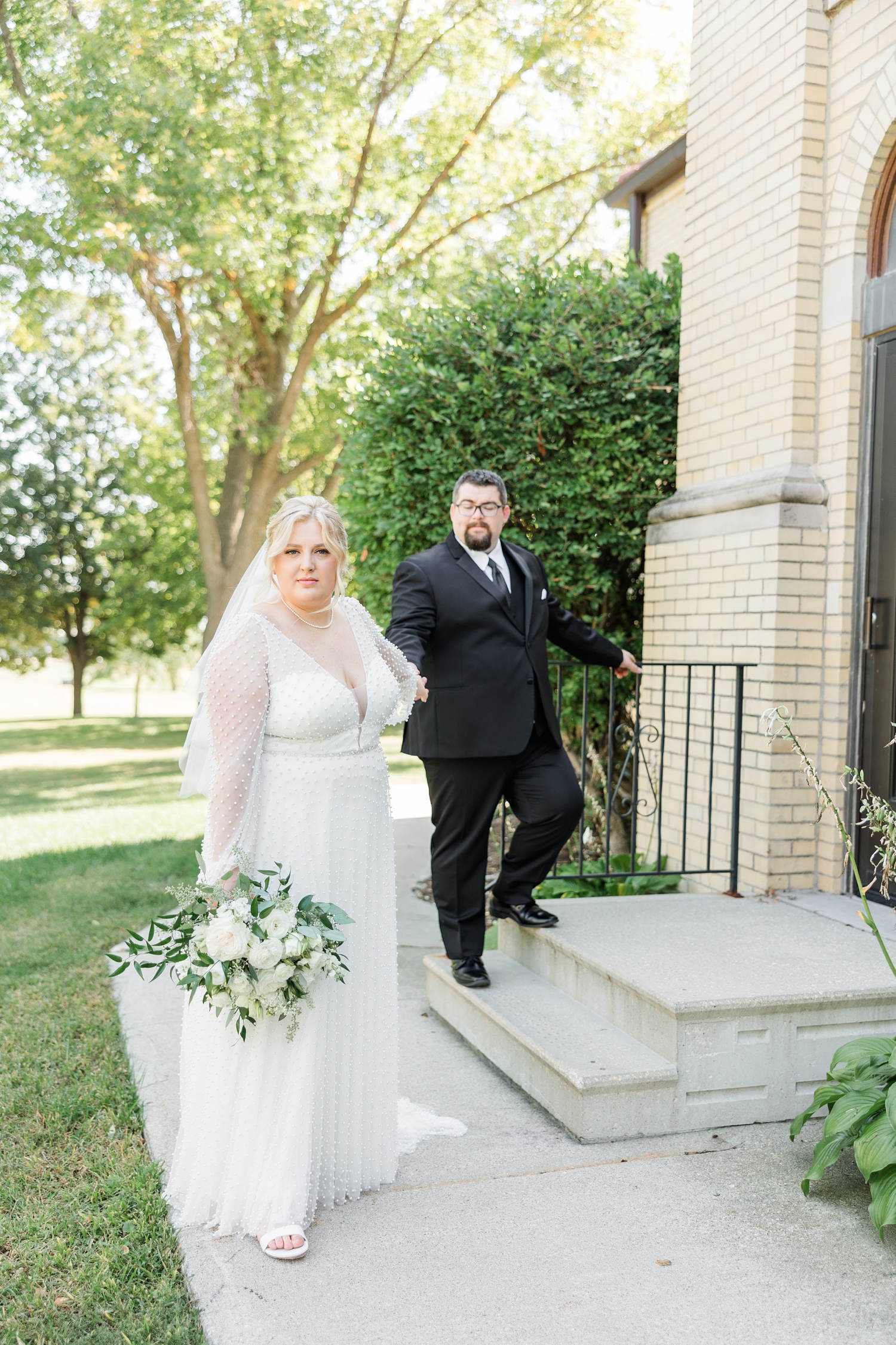 Halie leads her new husband, Nick, down a sidewalk at St. John the Baptist Catholic Church in Bancroft, IA | CB Studio