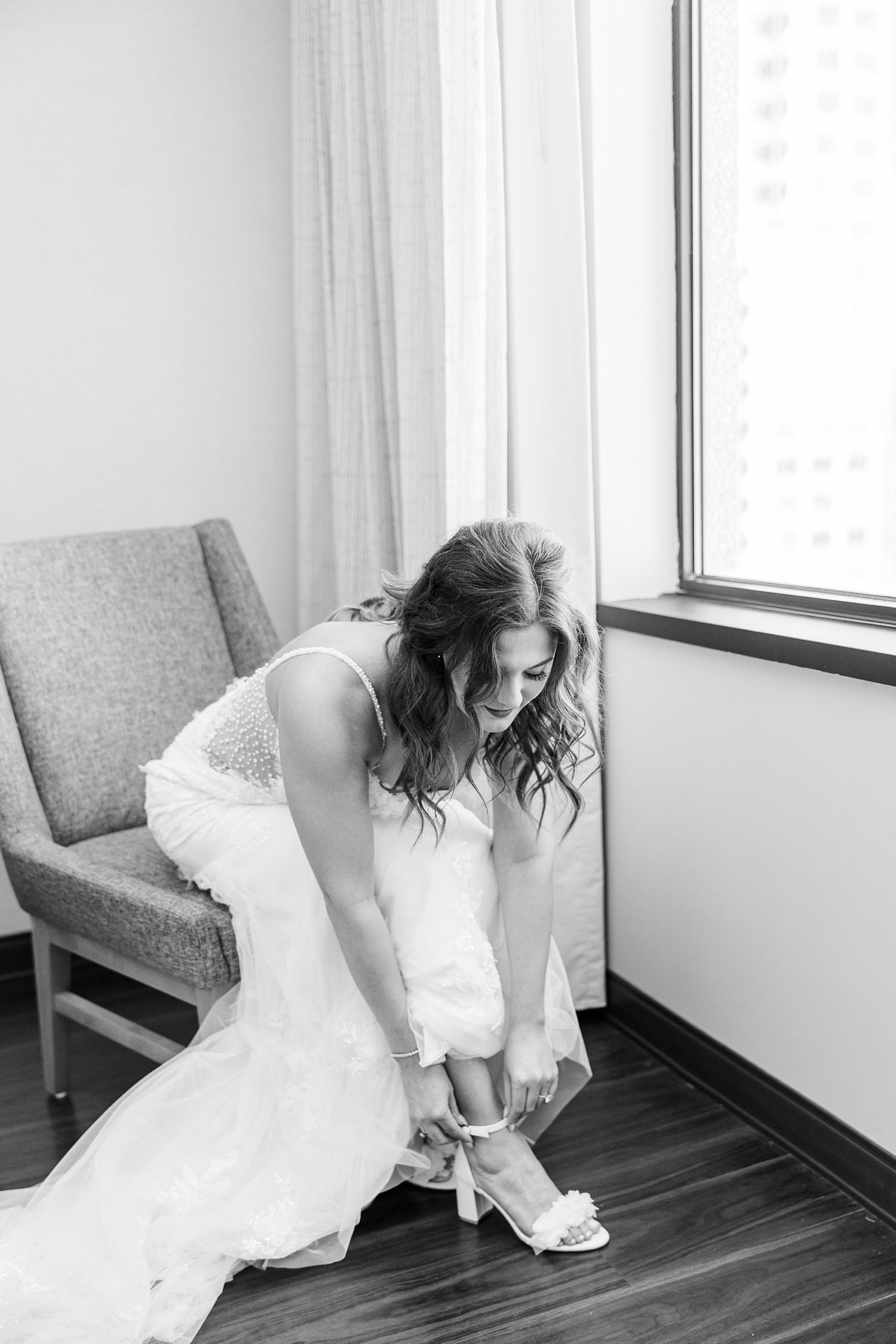 Jenna sits in a chair and adjusts the strap of her heel while getting ready for her wedding day in the bridal suite of the Downtown Des Moines Marriott | CB Studio