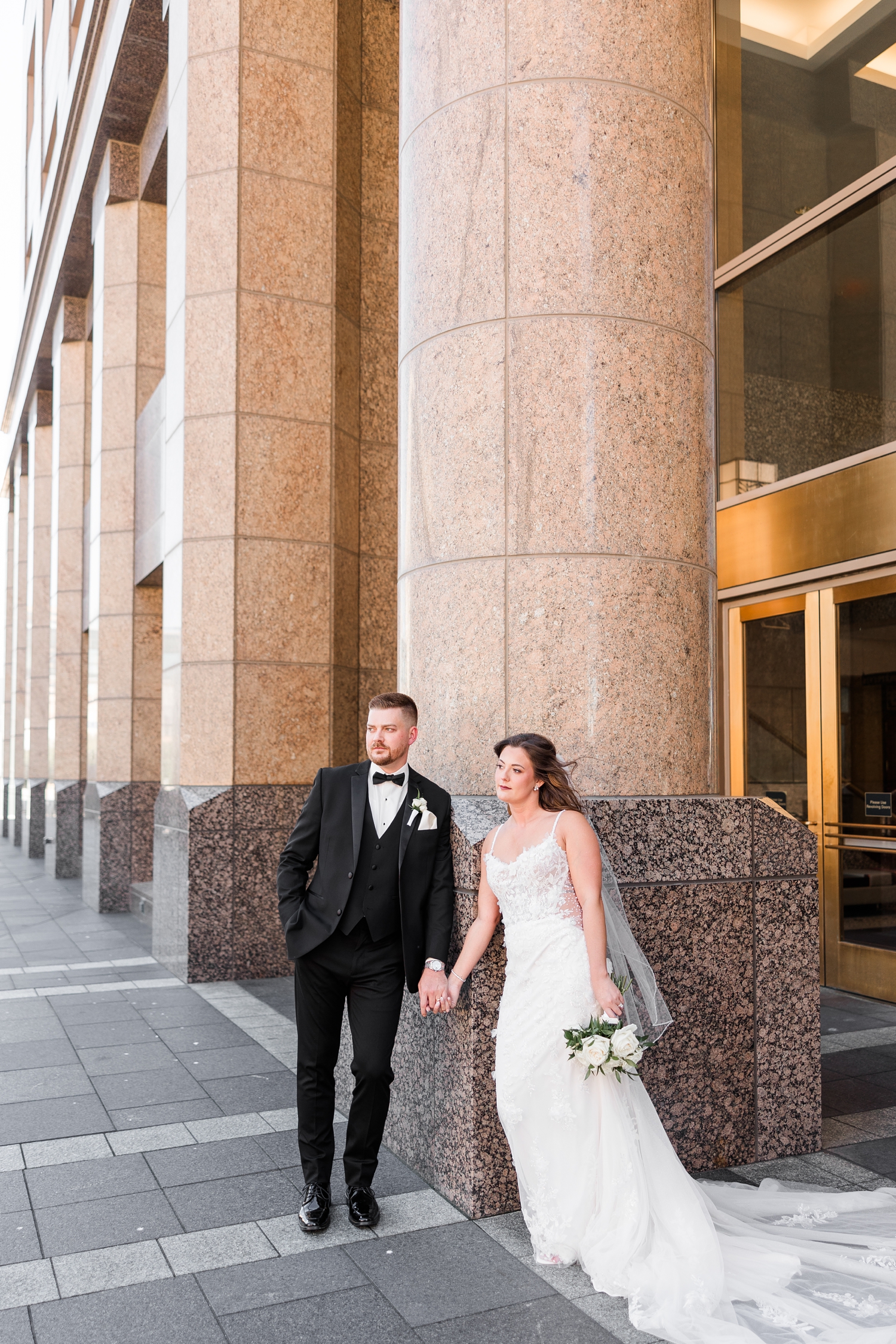 Dustin and Jenna hold hands and lean against a pillar on the back entrance of 801 Grand in downtown Des Moines | CB Studio