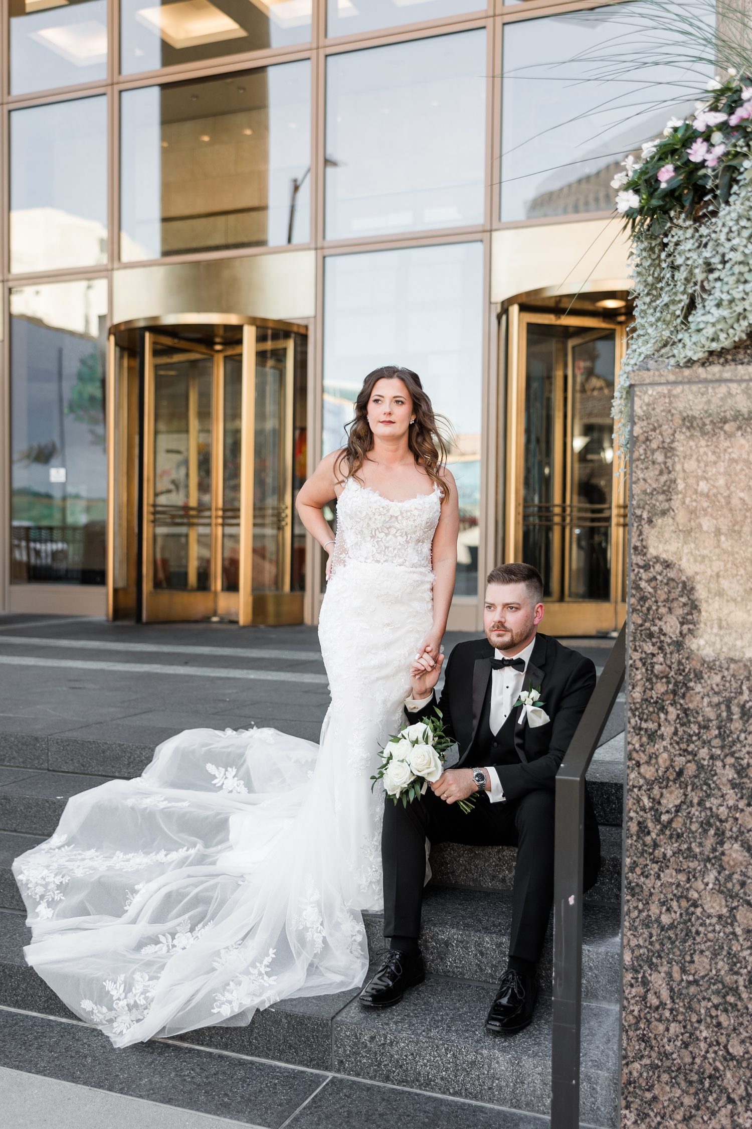 Dustin sits while Jenna stands and holds his hand on the steps of 801 Grand in downtown Des Moines | CB Studio