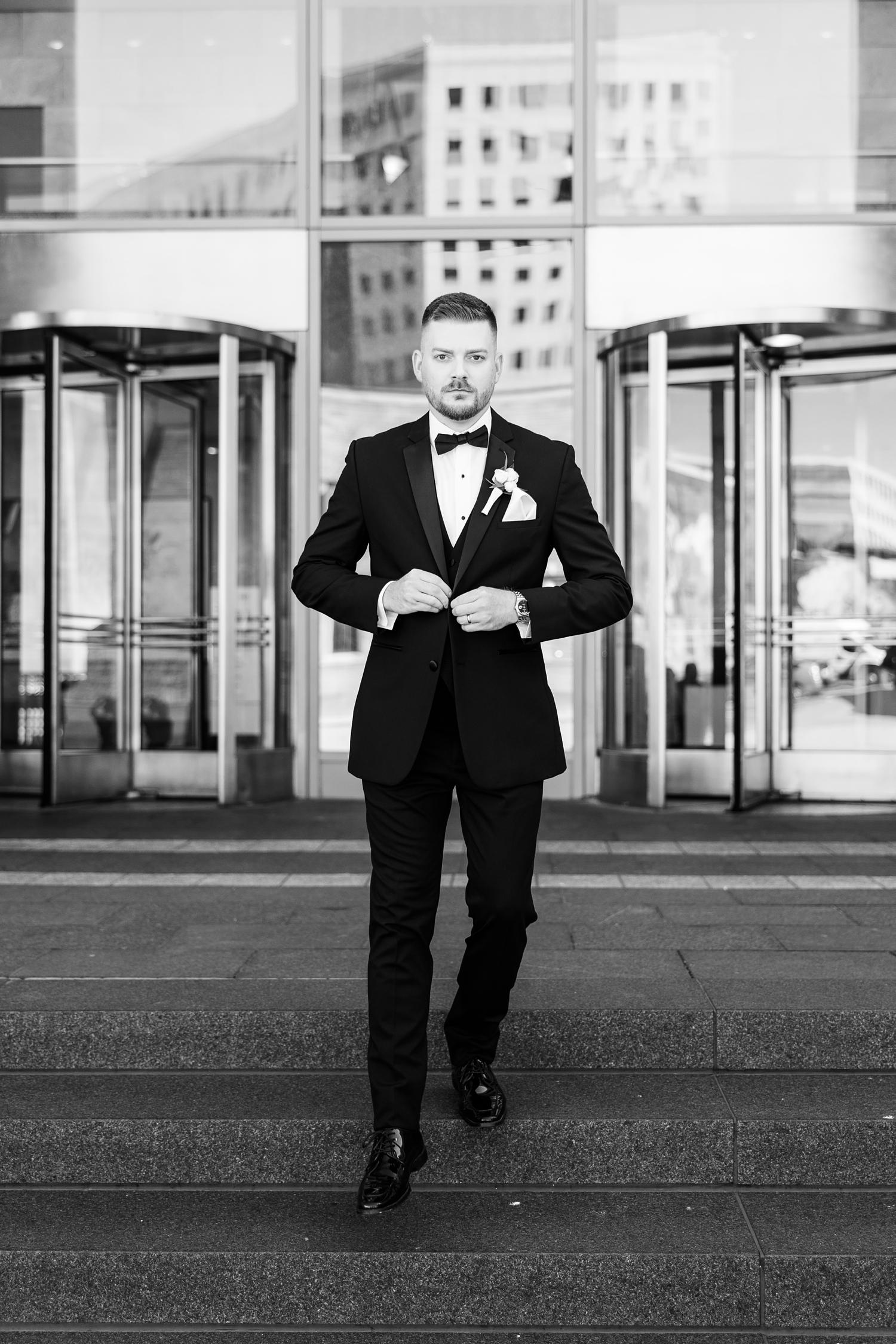 Dustin, dressed in full tuxedo, walks stoically down the steps of 801 Grand in downtown Des Moines while adjusting his suit jacket button | CB Studio