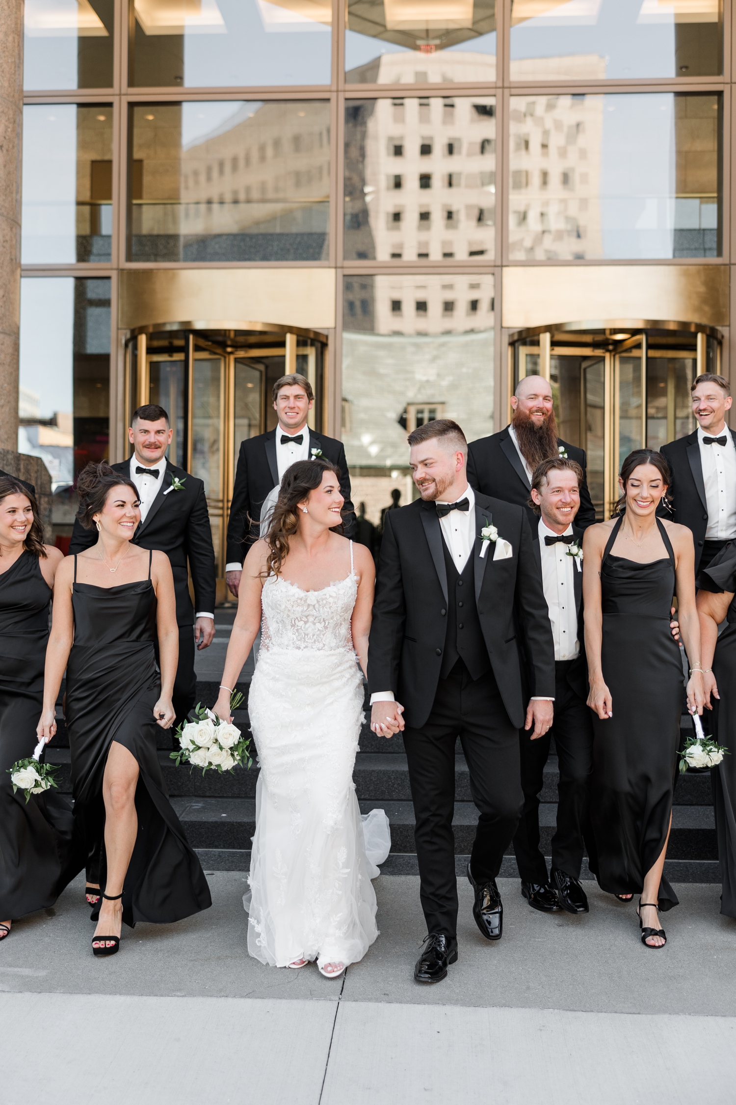 Jenna and Dustin walk hand and hand smiling down the steps of 801 Grand in downtown Des Moines with their wedding party | CB Studio