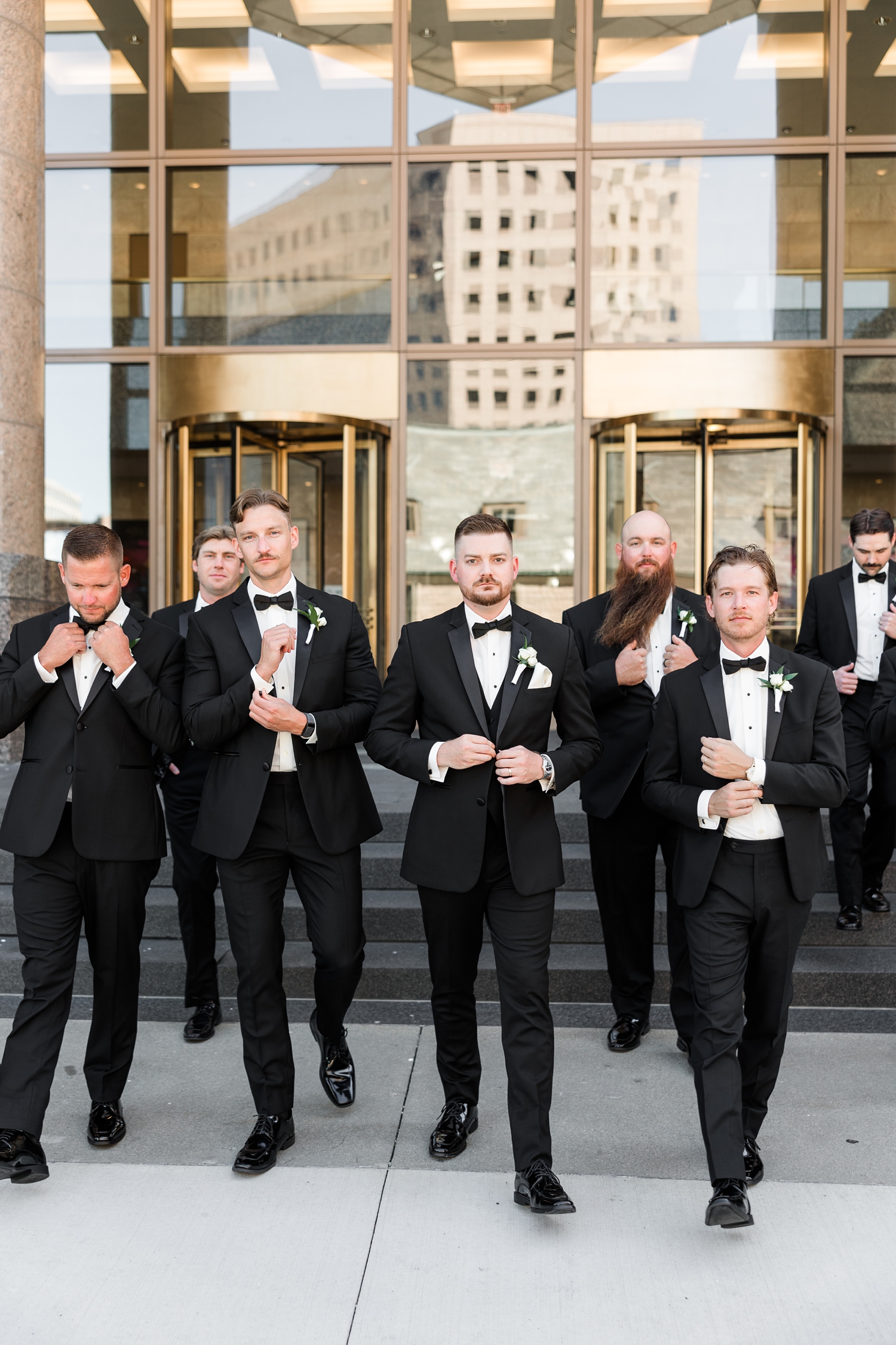 Dustin and his groomsmen stoically walk down the steps of 801 Grand in downtown Des Moines while adjusting buttons and cuff links | CB Studio