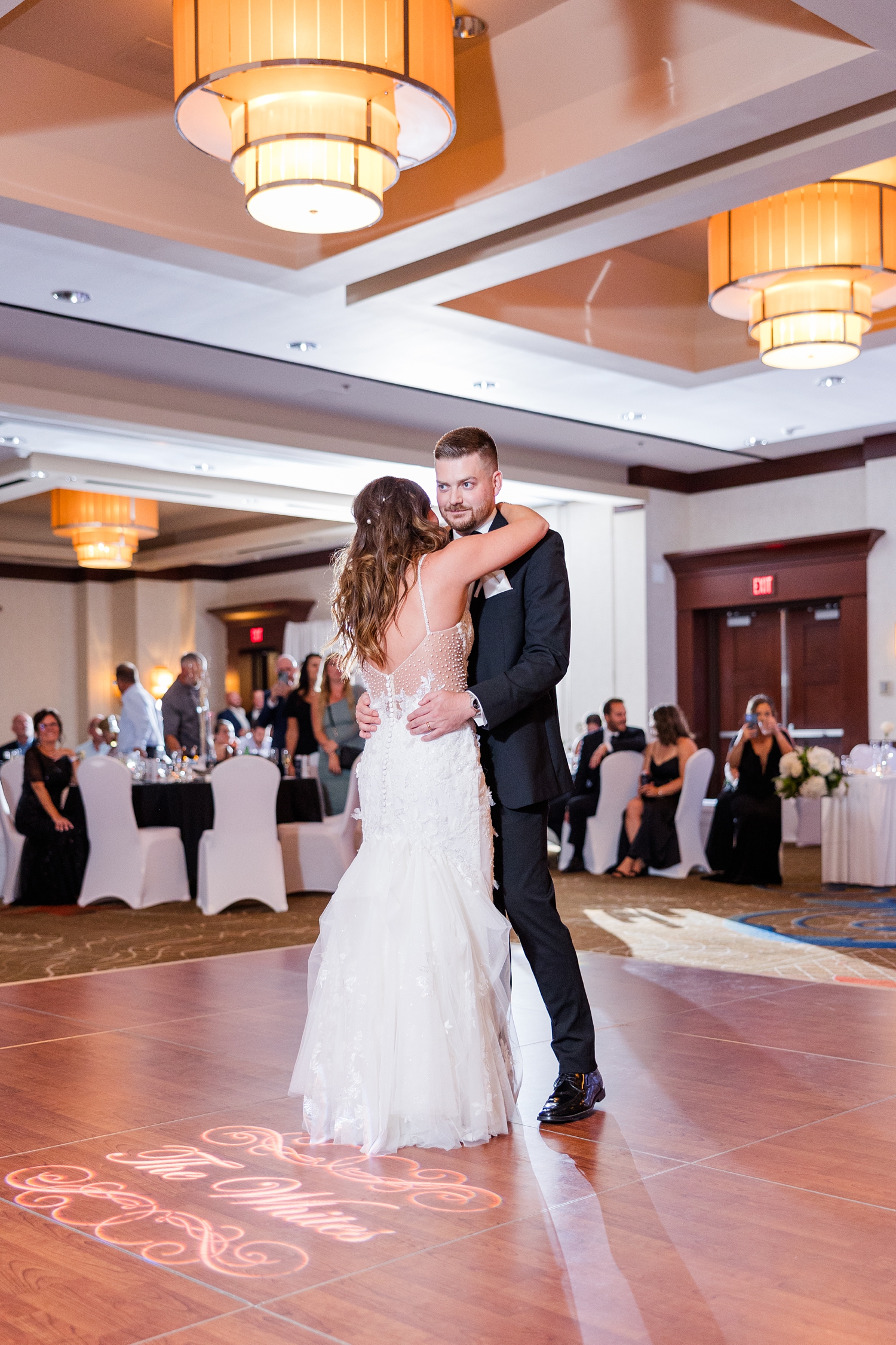 Jenna and Dustin share their first dance as husband and wife under a light that reads "The Whites" shining down on the dance floor at the Downtown Des Moines Marriott | CB Studio