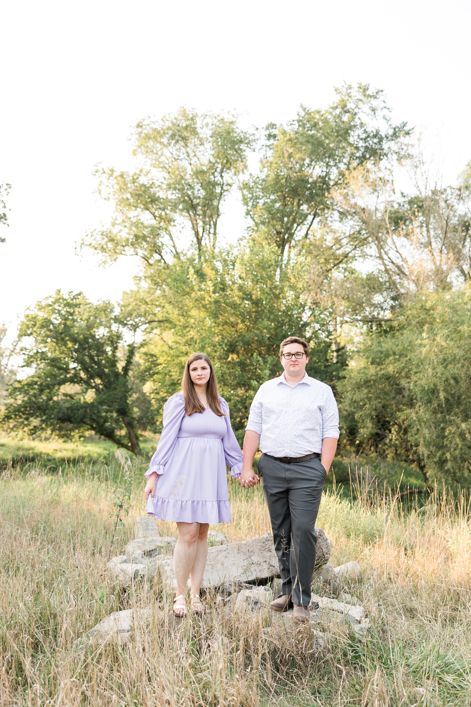 Myra and Kevin stand and hold hands on old concrete blocks in the middle of a grassy pasture | CB Studio