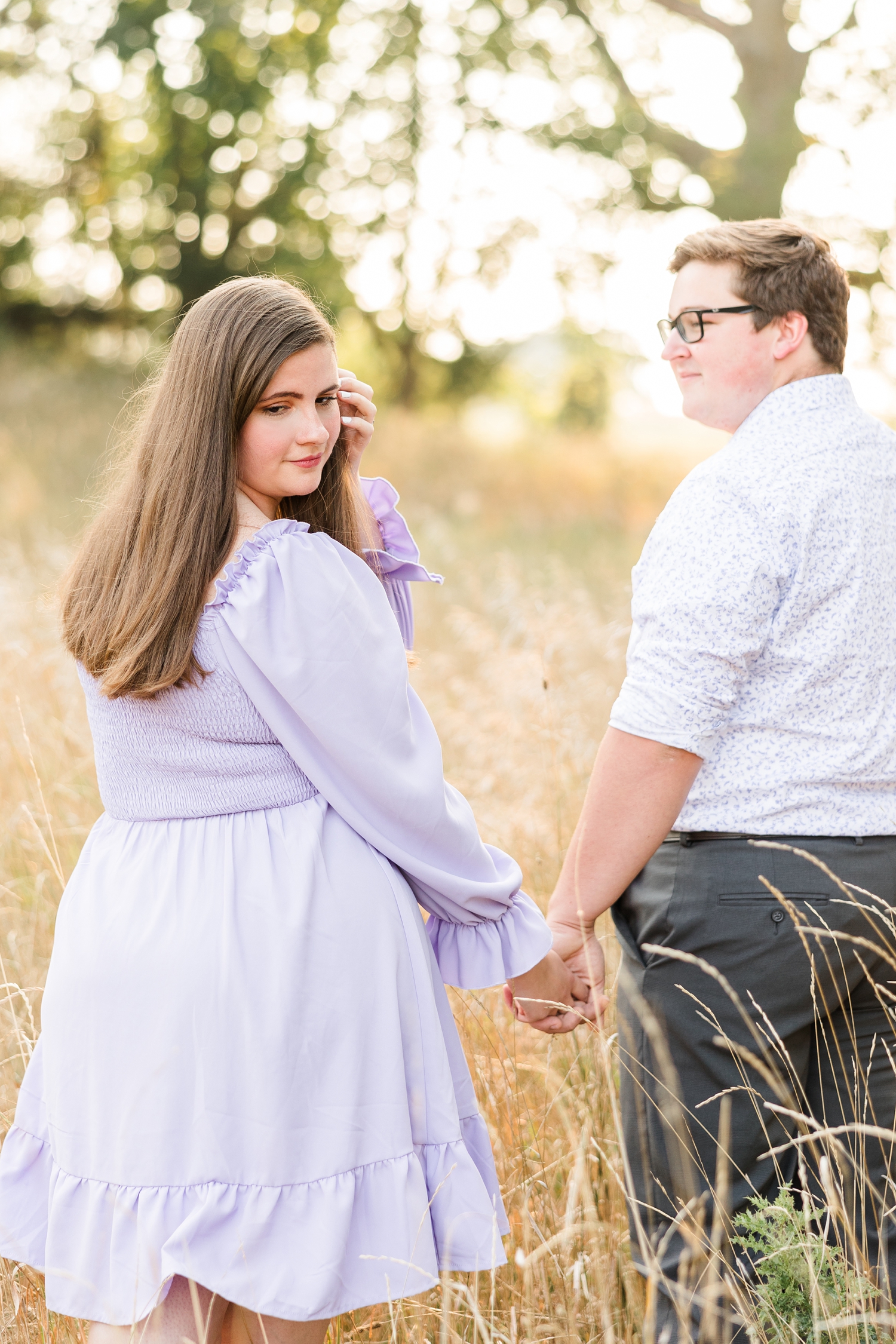 Kevin and Myra walk in a grassy pasture as Myra looks back and down and tucks her hair behind her ear | CB Studio