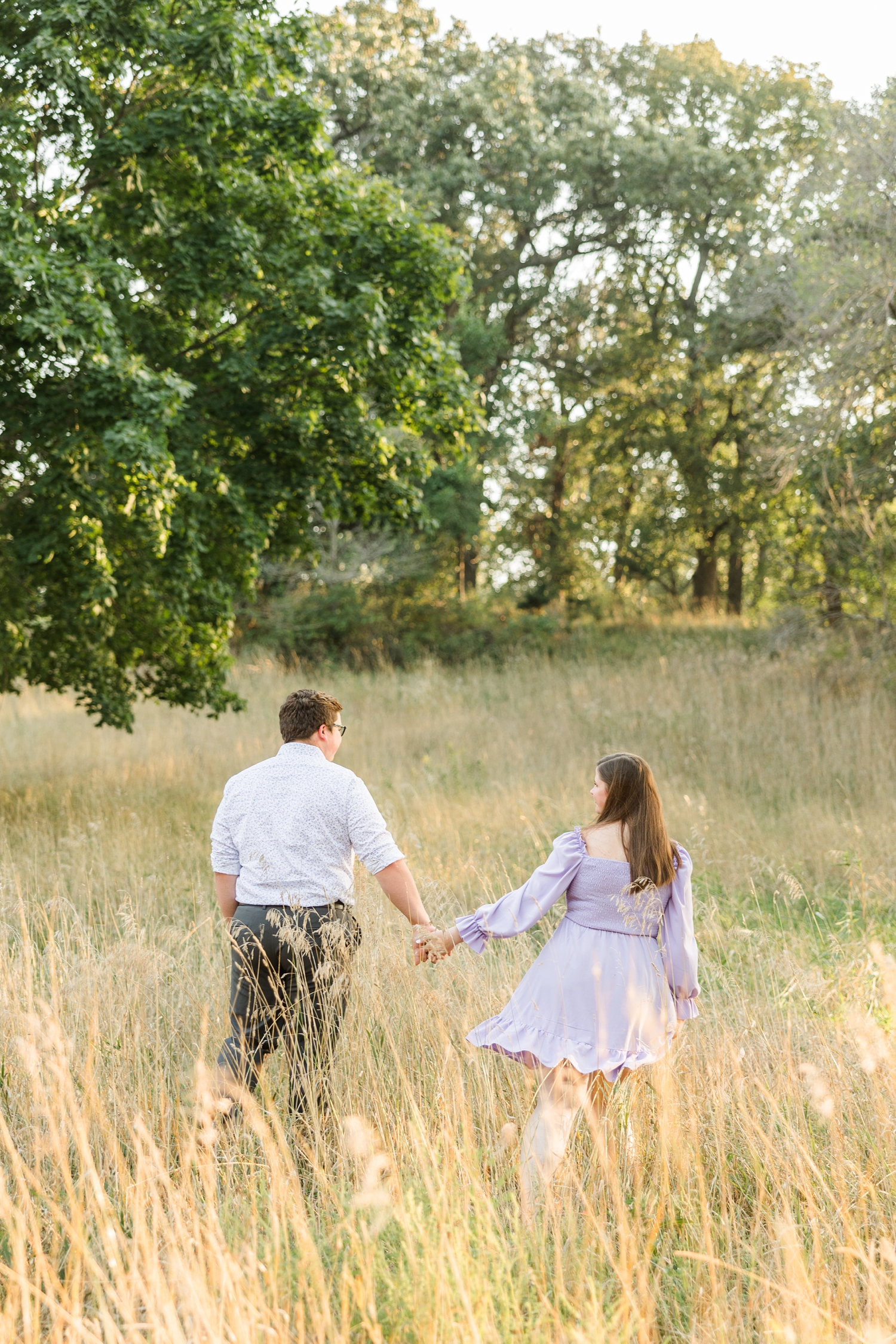 Kevin and Myra walk away up a hill to the oak trees in a grassy pasture while holding hands | CB Studio