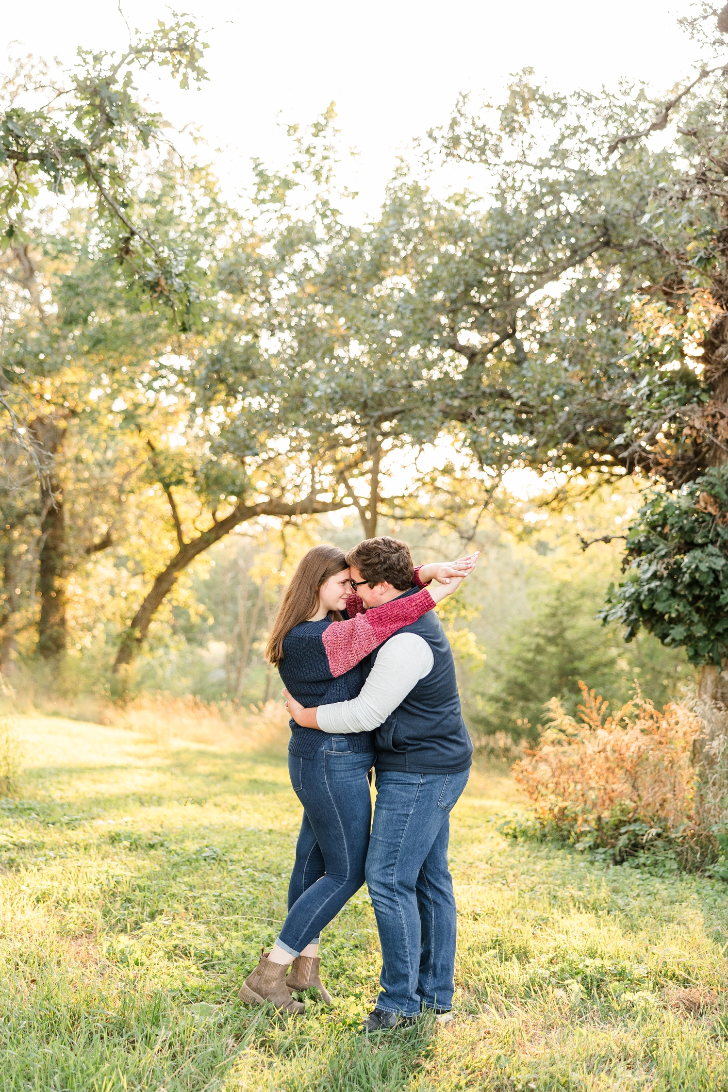 Kevin and Myra stand embracing each other in the middle of a grassy pasture surrounded by oak trees at beautiful, glowy golden hour | CB Studio