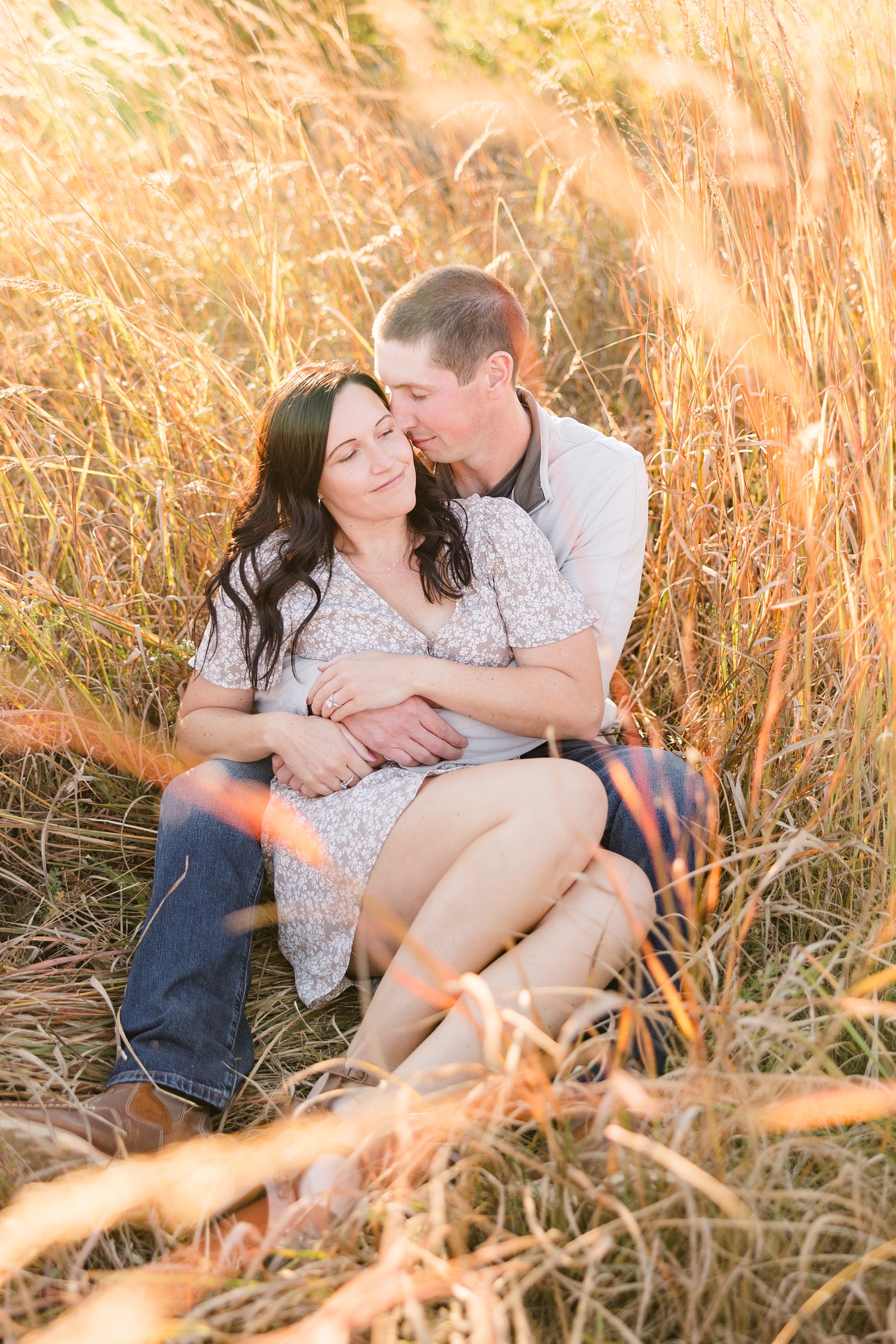 Brandon and Haley sit together in a grass field surrounded by orange fall grass as Brandon nuzzles Haley gently, located in Osage IA | CB Studio