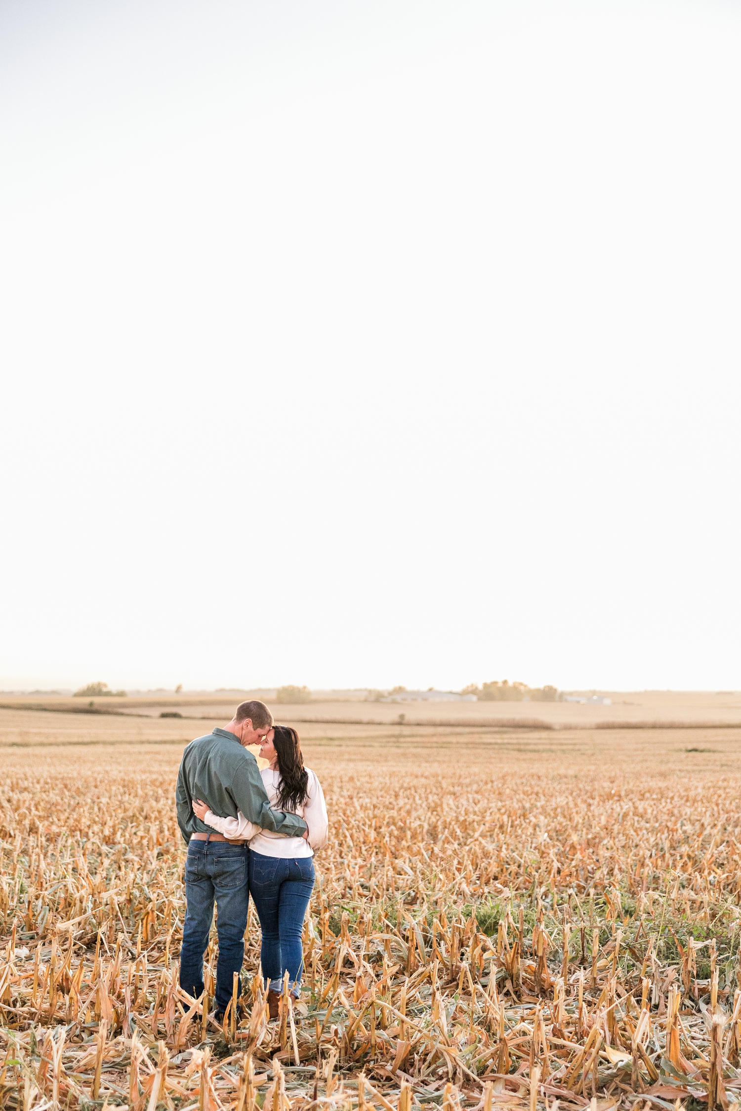 Brandon and Haley stand side by side in a freshly harvested corn field as they rest their foreheads together, located in Osage IA | CB Studio