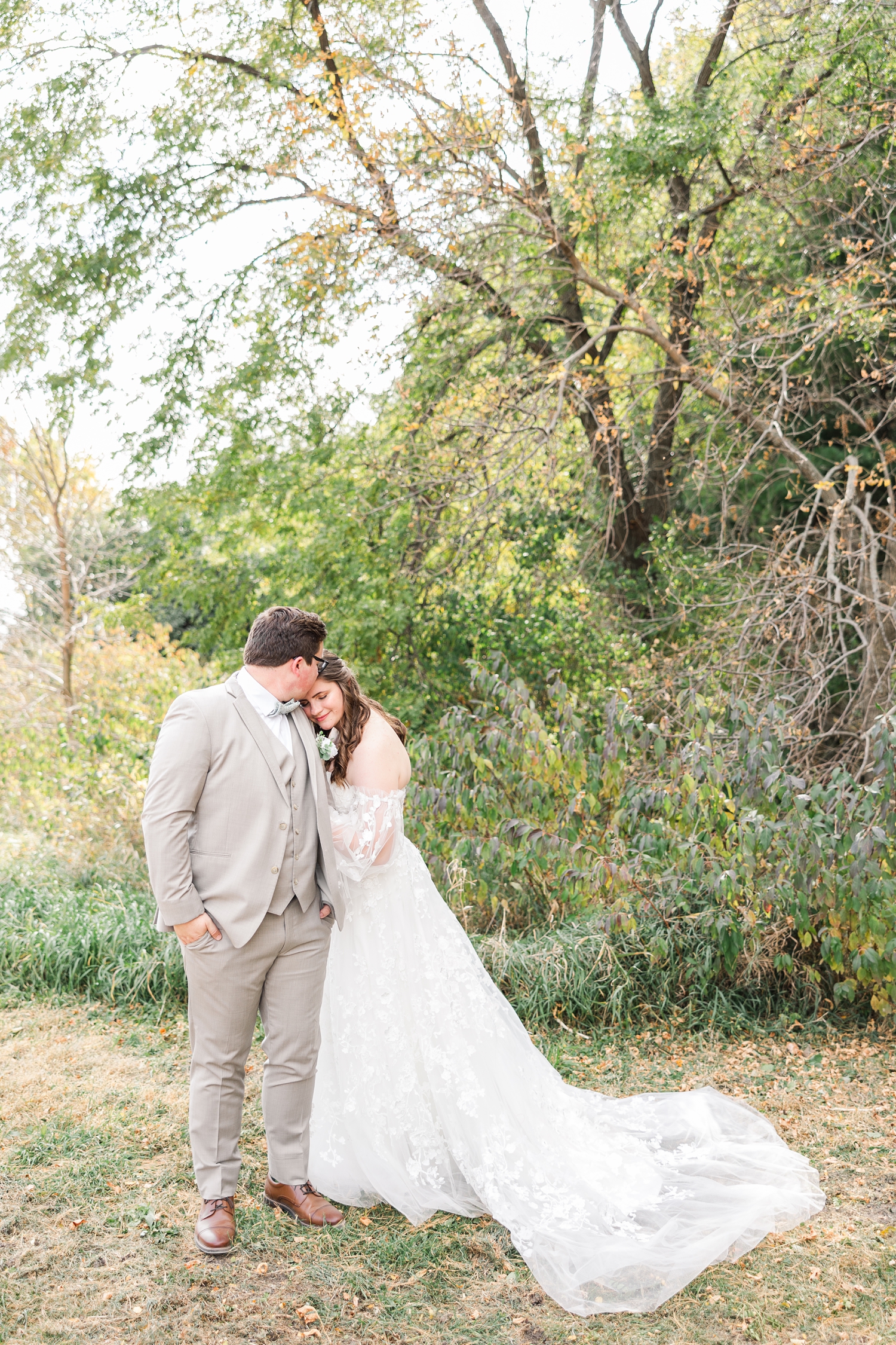 Myra, hugging Kevin's arm, rests her cheek on his shoulder and looks down, while Kevin kisses her forehead | CB Studio