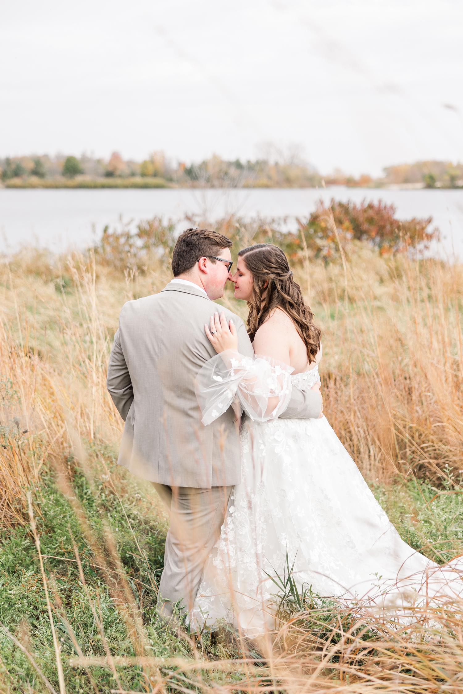 Kevin and Myra stand in tall fall grass as they touch noses, overlooking a scenic view of Smith Lake at Water's Edge Nature Center | CB Studio