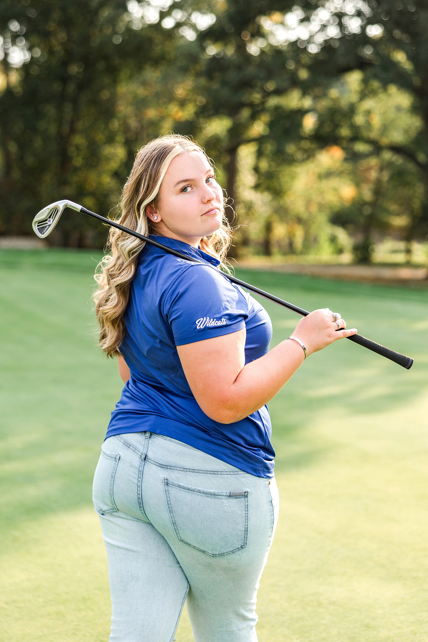 Shelby holds her golf club over her shoulder as she turns to look back behind her on the Humboldt golf course | CB Studio