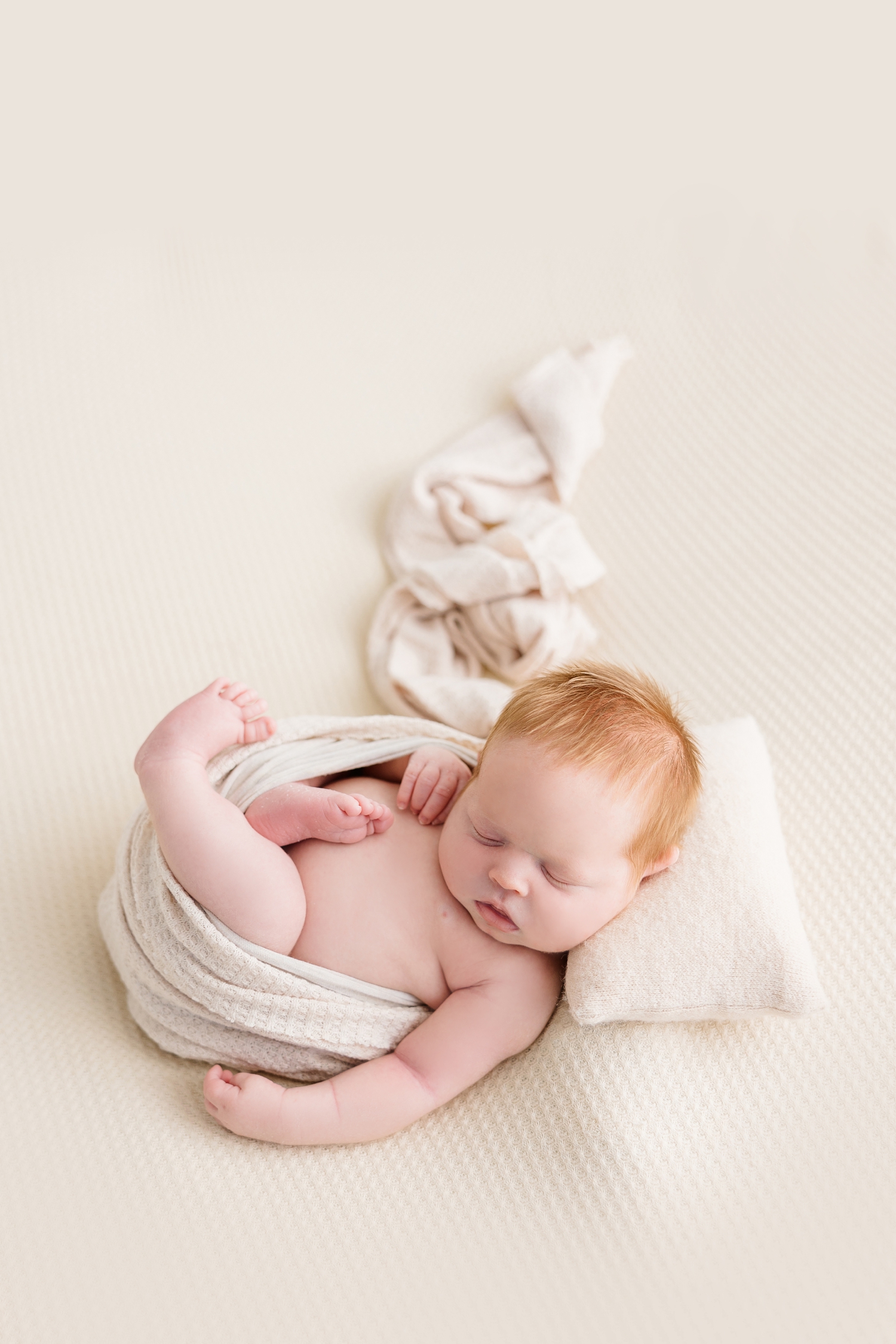 Baby Joey wrapped in neutral with his arms and legs free sleeps on a neutral background | CB Studio