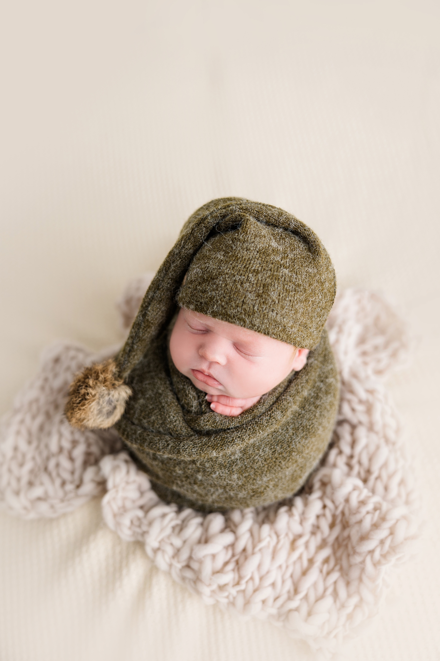 Baby Joey wrapped in green wool and wearing a green night cap is wrapped in a potato sack pose and sits on a neutral background | CB Studio