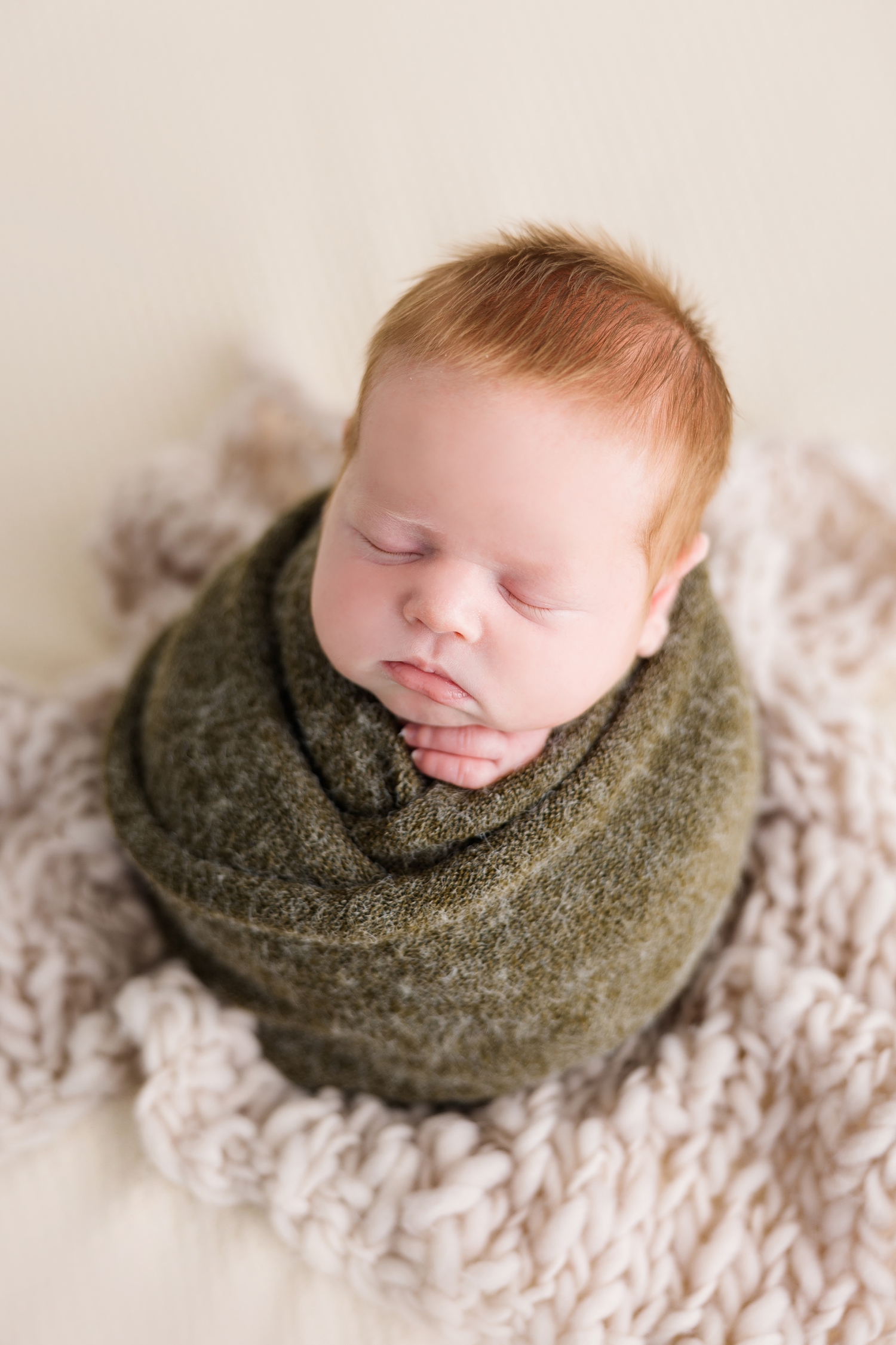 Baby Joey wrapped in green wool in a potato sack pose sits on a neutral background | CB Studio