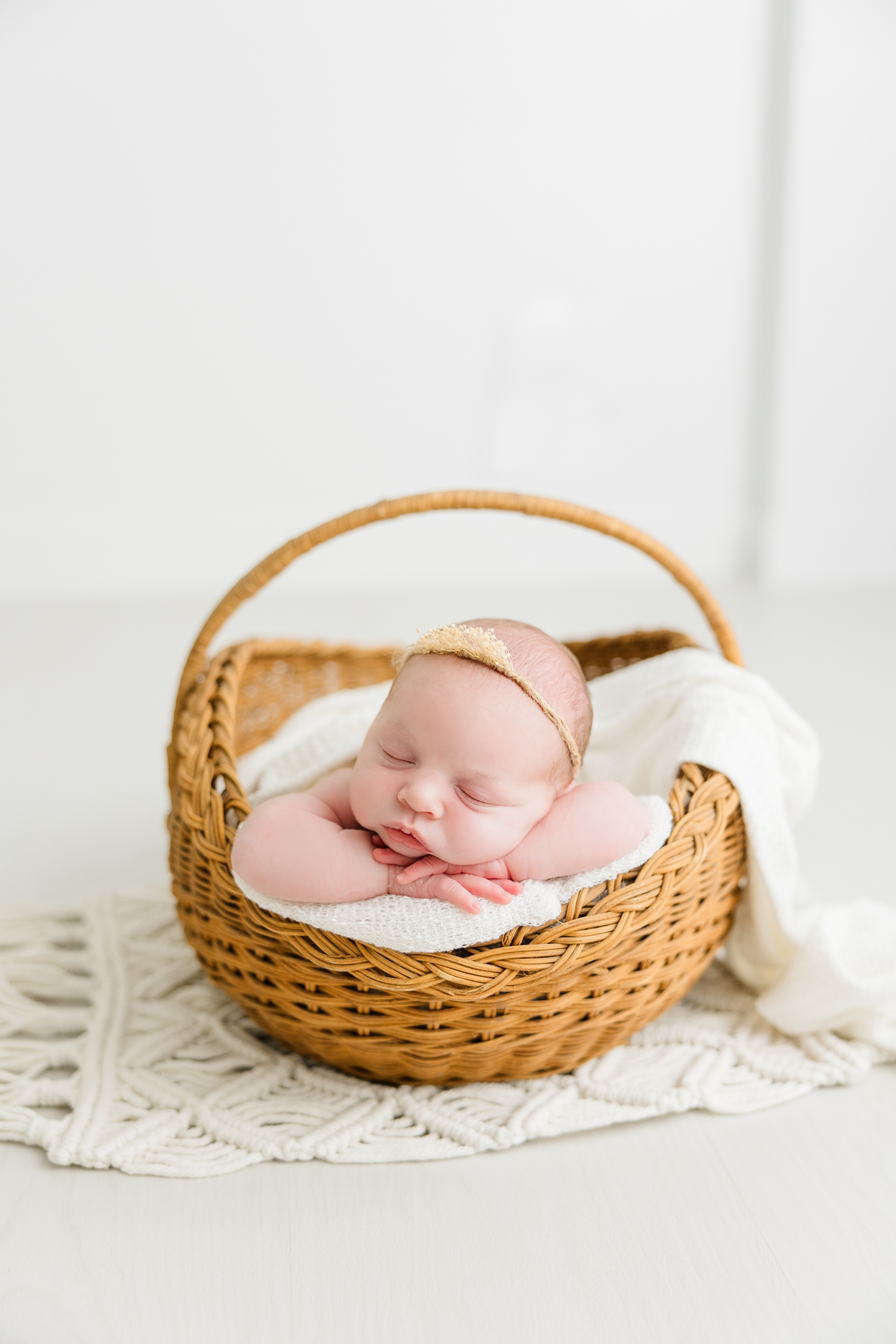 Baby Sadie nestled in a wicker basket on top of a white macrame rug in a white room | CB Studio