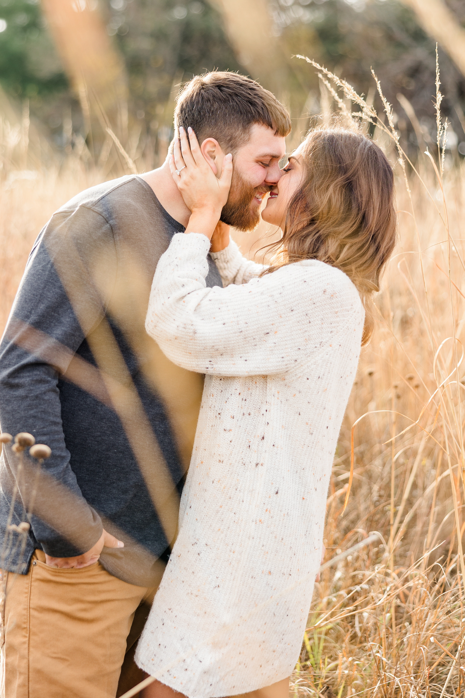 Kylie holds Drake's cheeks as she pulls him in for a kiss while smiling all while standing in a grass field in the fall | CB Studio