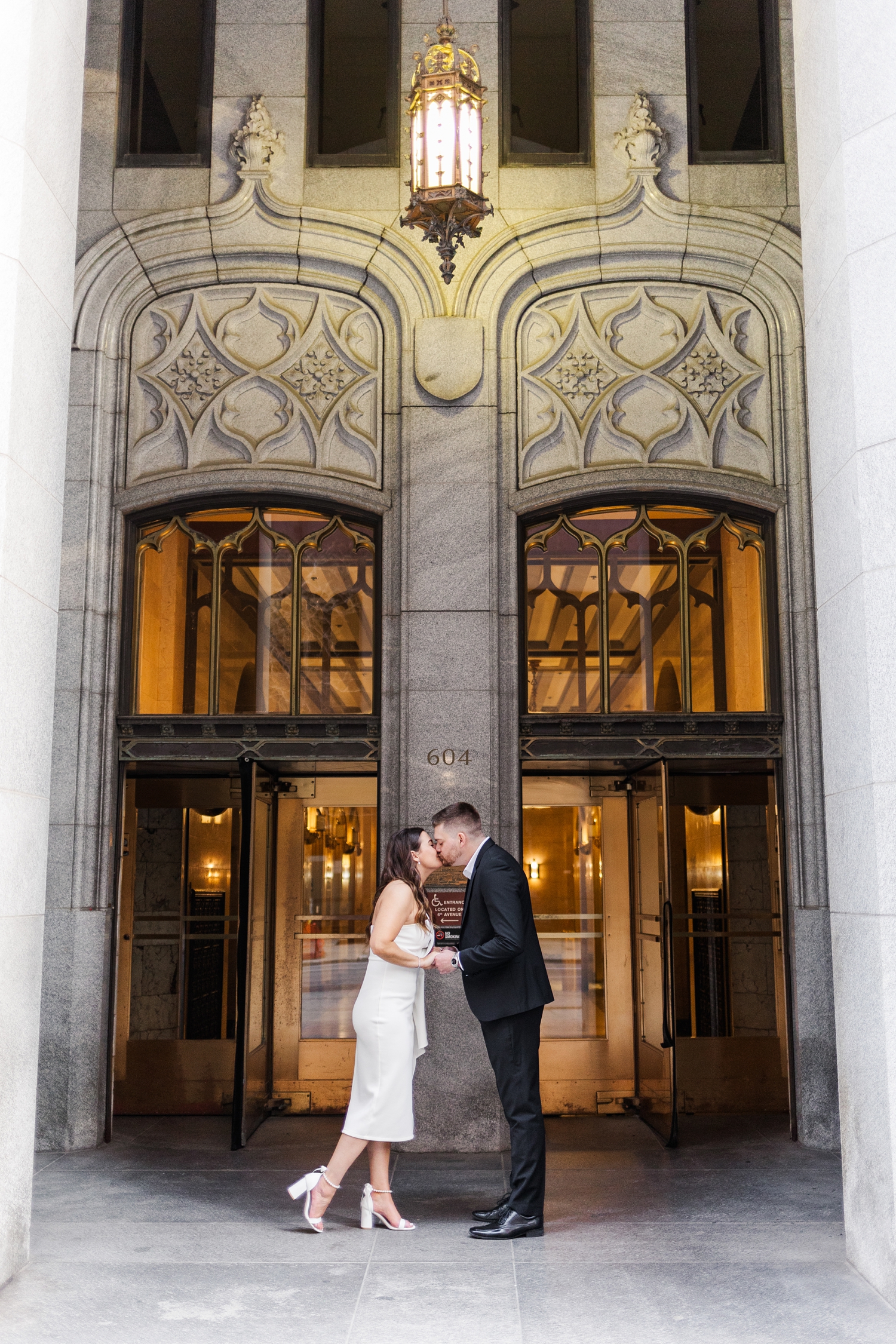 Best of 2024 Engagements | Jenna and Dustin face each other while holding hands and lean in for a kiss in front of the beautiful architecture of the The Equitable Building in Des Moines, IA | CB Studio