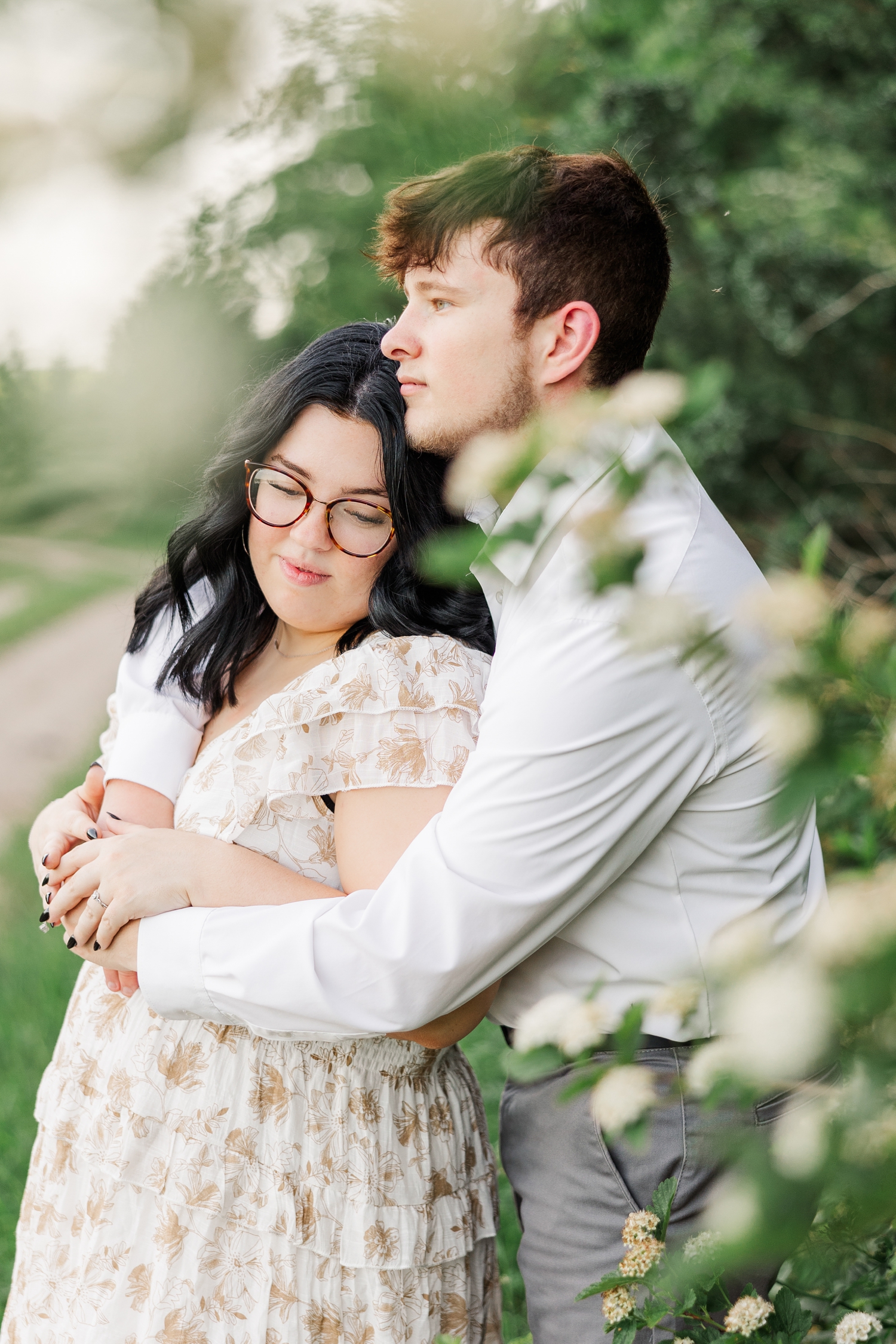 Best of 2024 Engagements | Brandon embraces Kylie from behind as they are surrounded by white spring blooms | CB Studio