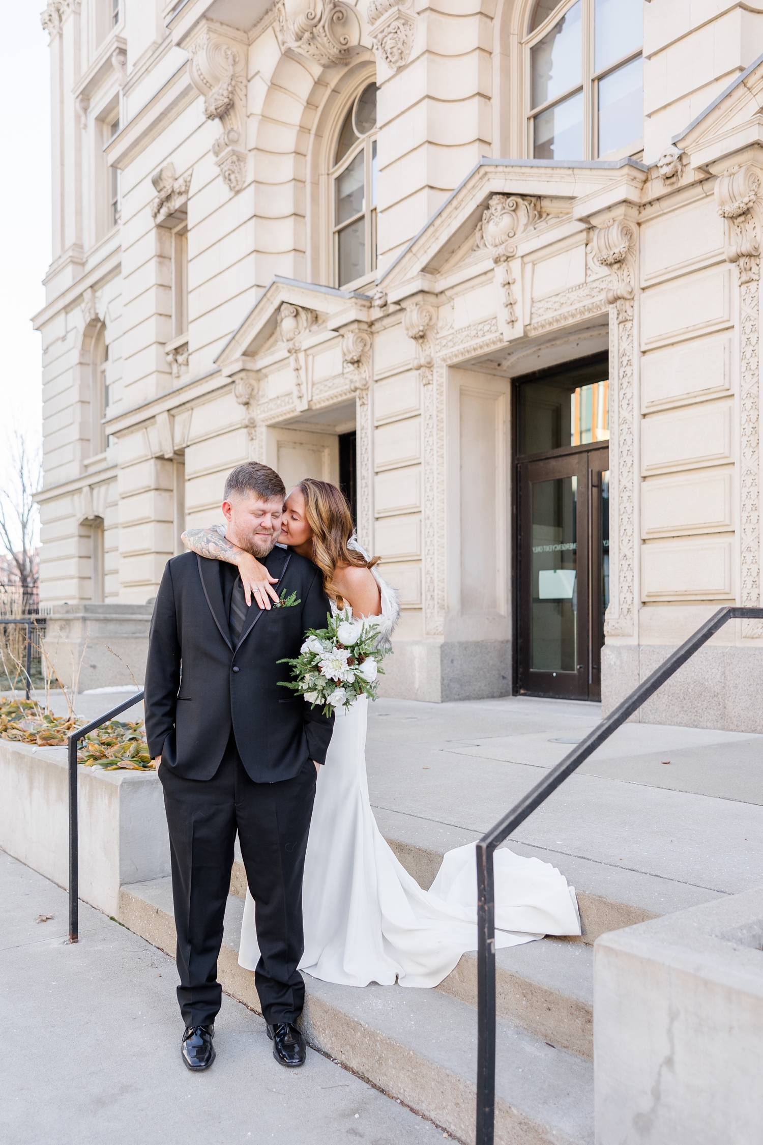 Lisa wraps her arm around Chris and leans in to kiss him on the cheek on the steps of the Polk County Courthouse | CB Studio