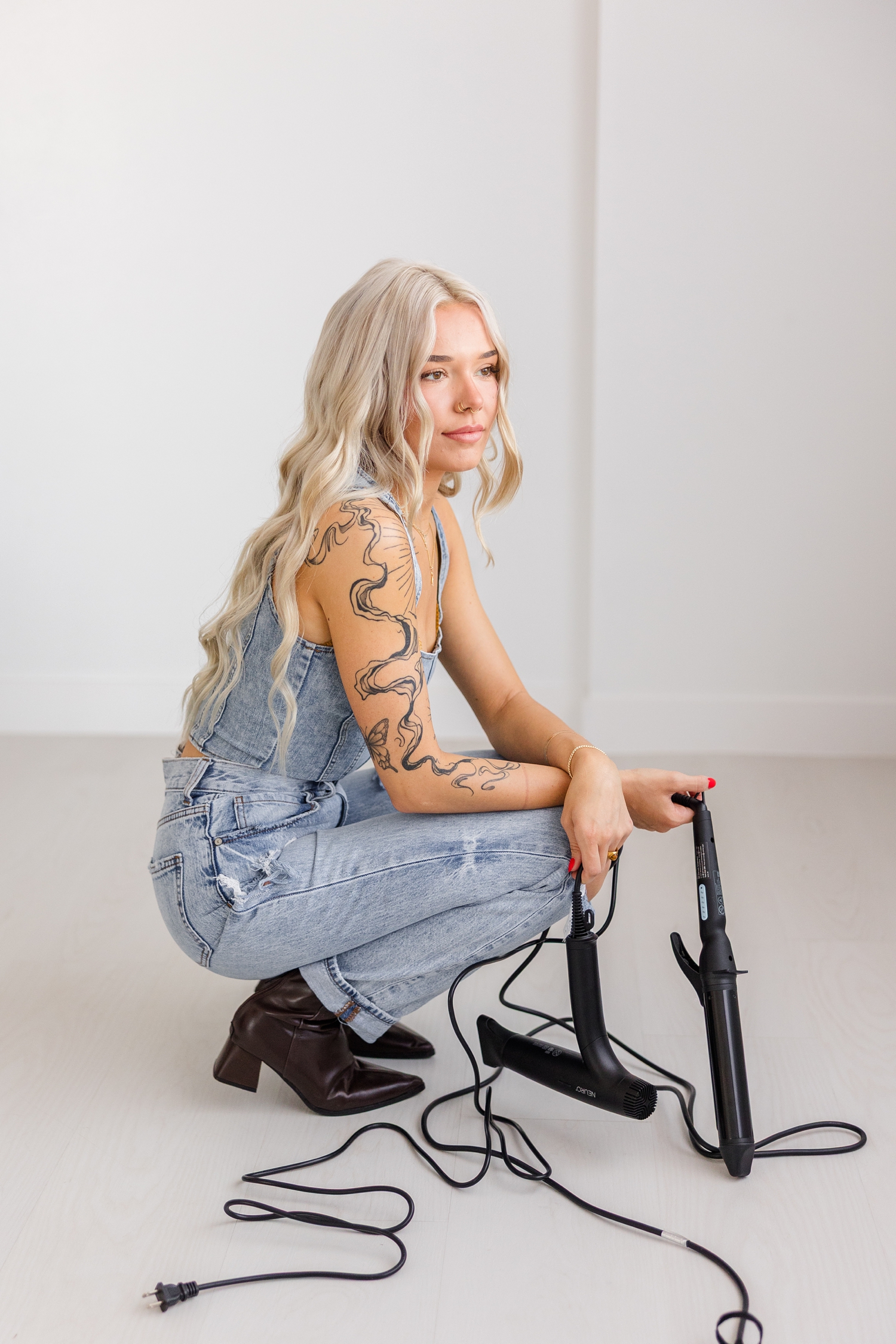 Hairstylist, Addi, squats in a white room on the floor holding her two favorite hot tools | CB Studio