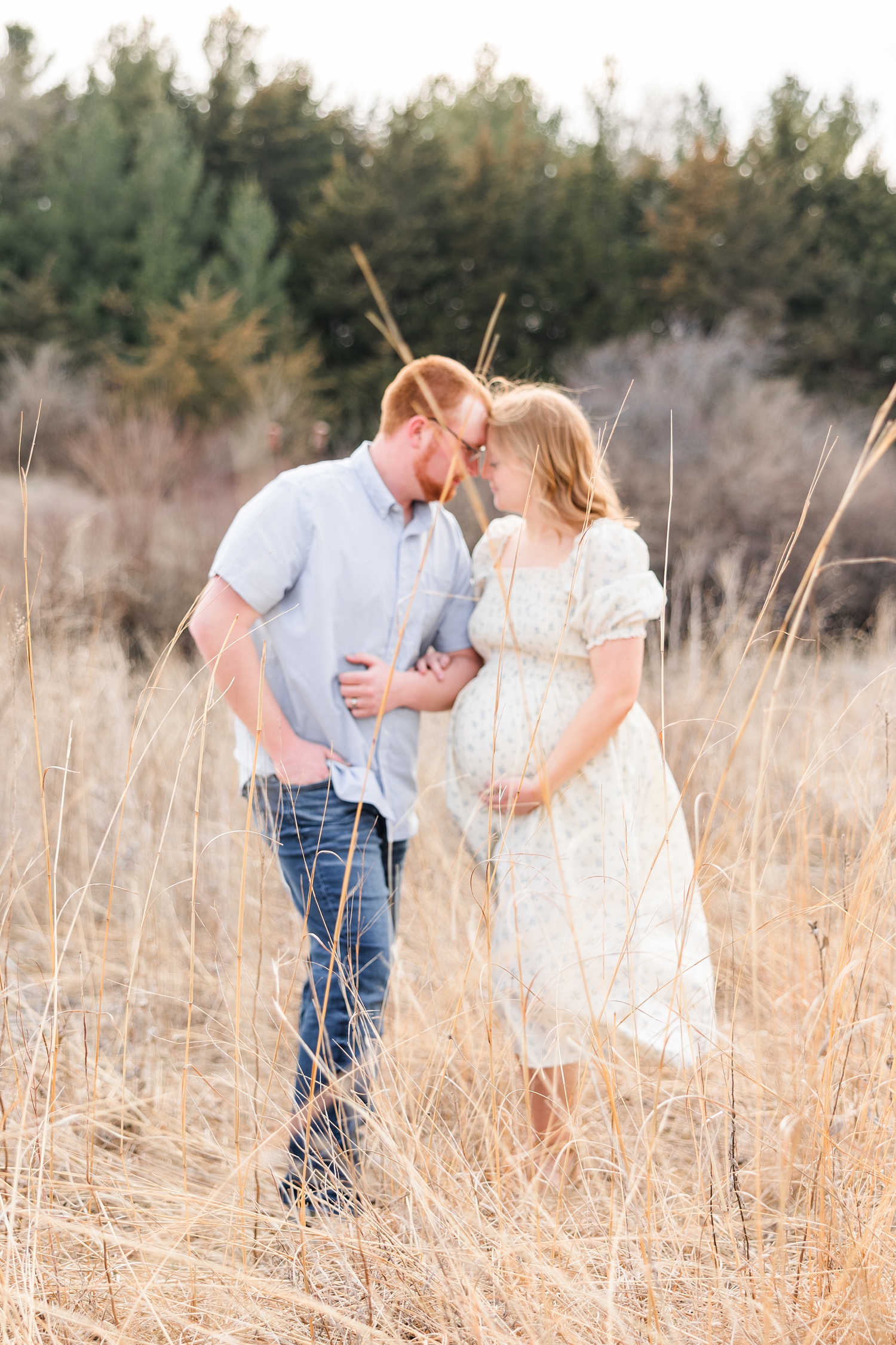 Matt and Lauryn stand in a grass field resting their foreheads together as Lauryn hugs her baby belly | CB Studio