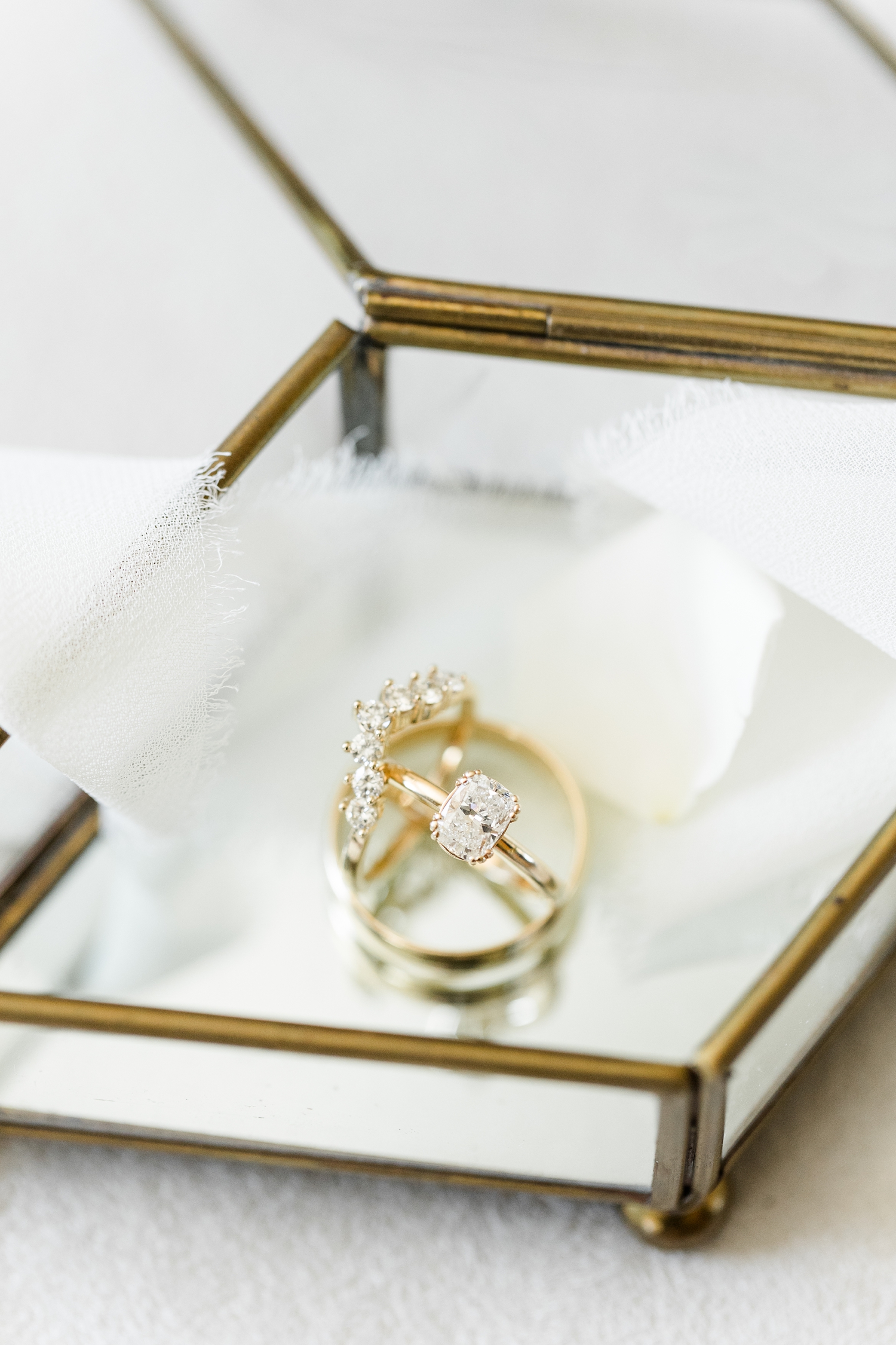Antique cushion diamond engagement band set in a gold vintage inspired setting paired with V-shaped diamond wedding band and a gold men's wedding band displayed in an old antique mirrored box with a white chiffon ribbon swirling through it | CB Studio