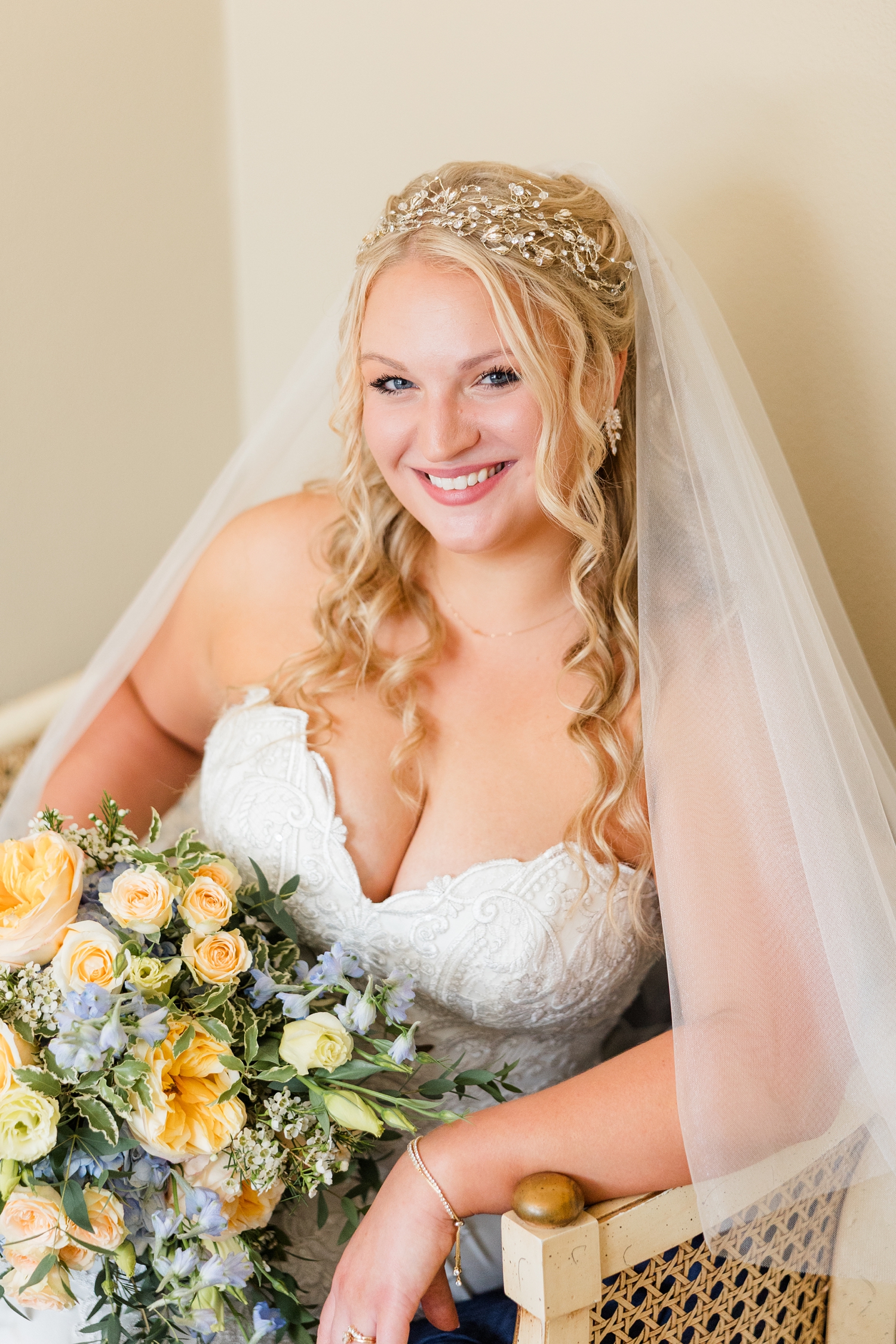 Natalie, complete in her bridal look, including a Casablanca wedding gown, sits on a navy vintage bench while holding her wildflower inspired bouquet featuring peach garden roses, blue hydrangeas, small cream roses and blue delphinium | CB Studio