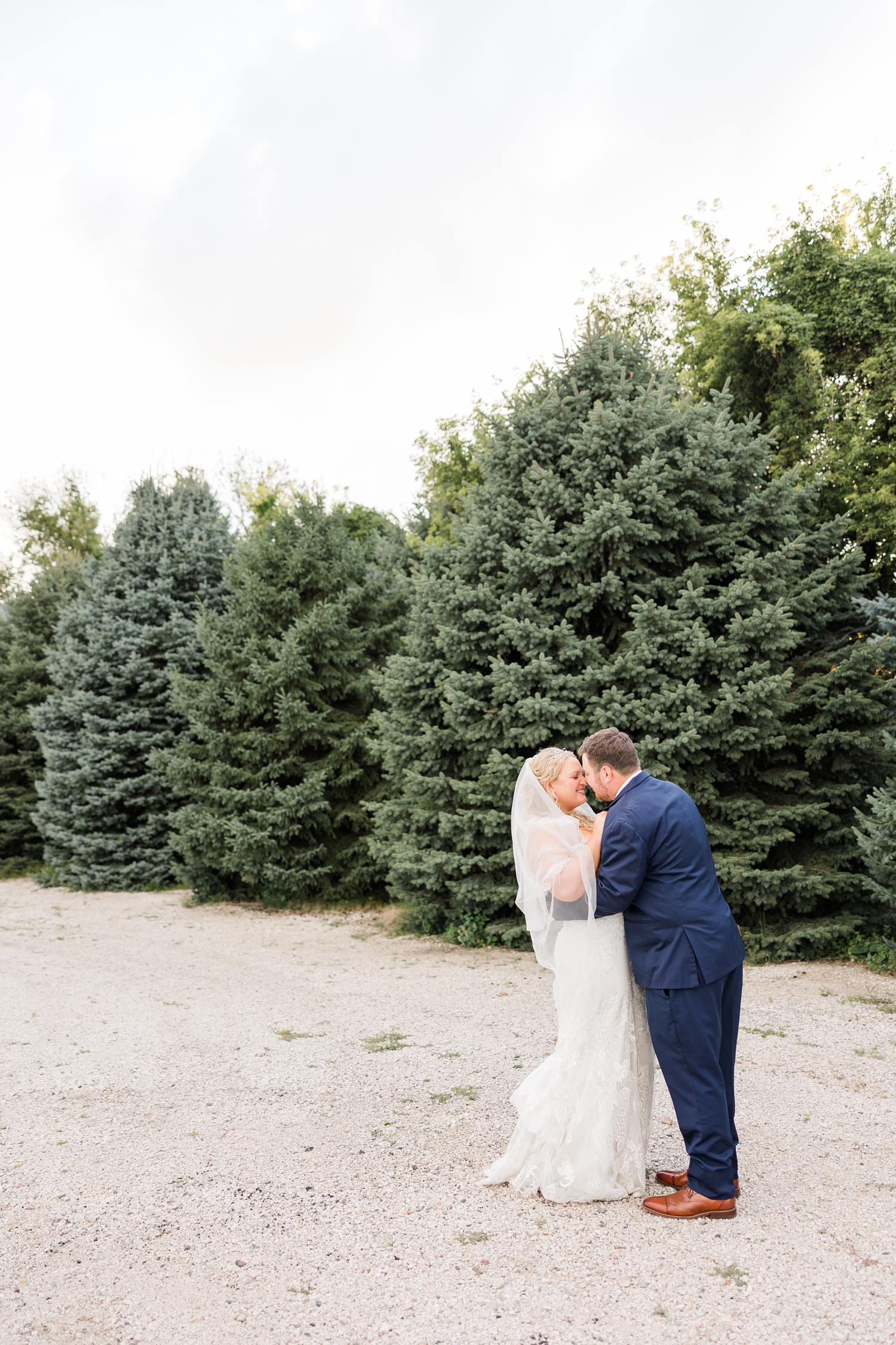 Natalie and Connor touch noses and Connor slight dips Natalie back in front of an evergreen tree line at sunset | CB Studio