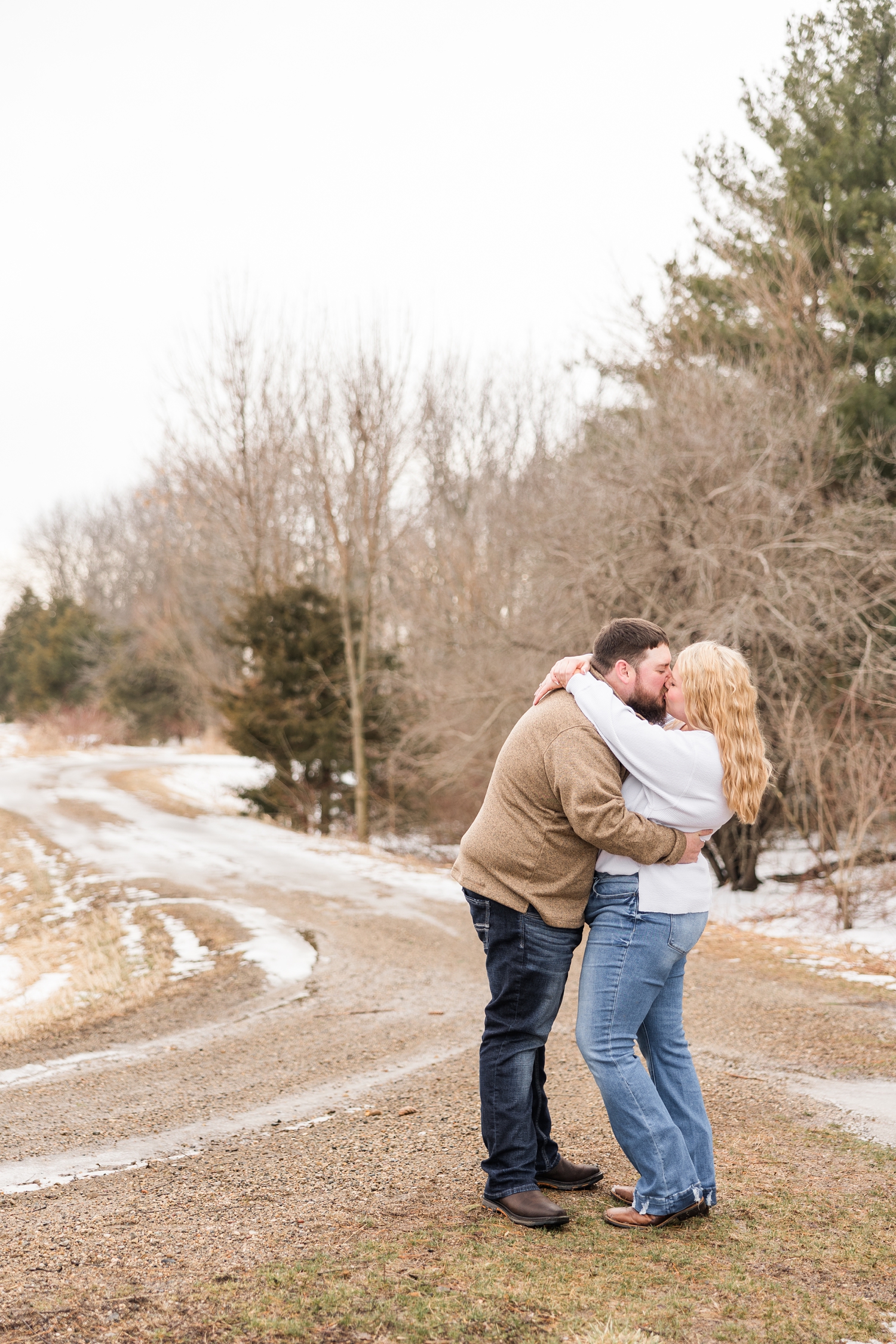 Dalton and Teri embracing and sharing a kiss along a curvy path at Water's Edge Nature Center during early spring in Iowa | CB Studio