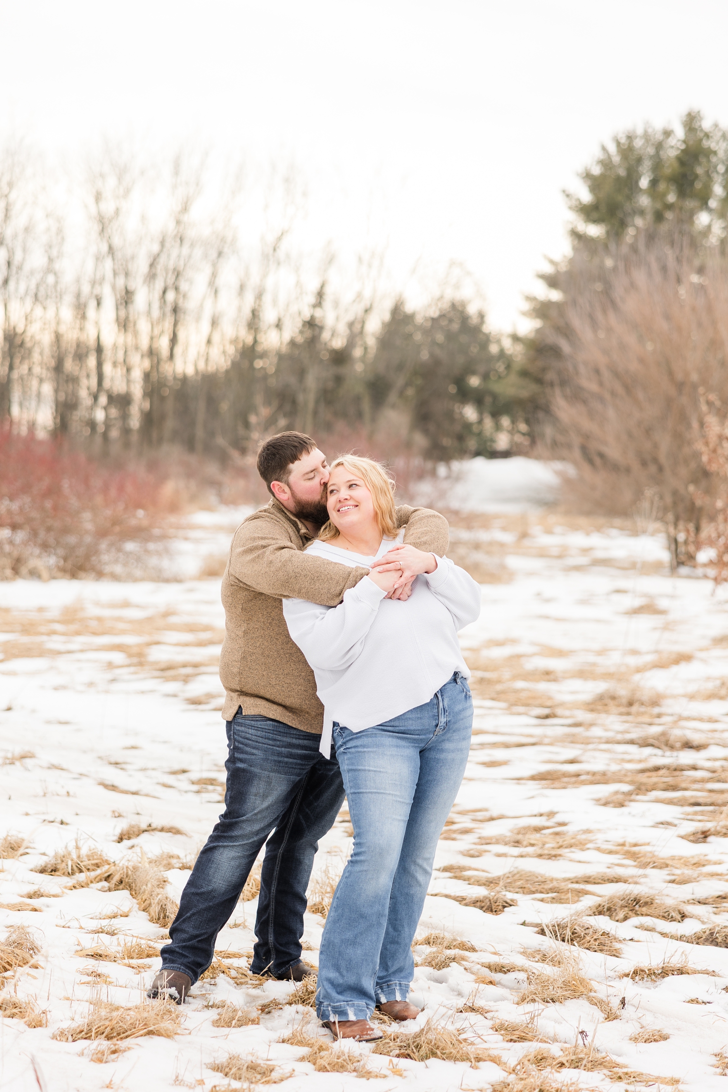 Dalton embracing Teri from behind and kissing the side of her head at Water's Edge Nature Center during early spring in Iowa | CB Studio