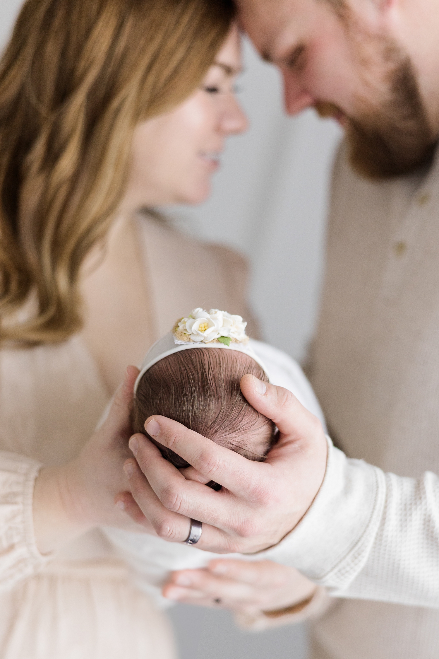 Andrea and Josh rest their foreheads together while holding baby Parker up, head first, with focus on their hands holding her head | CB Studio
