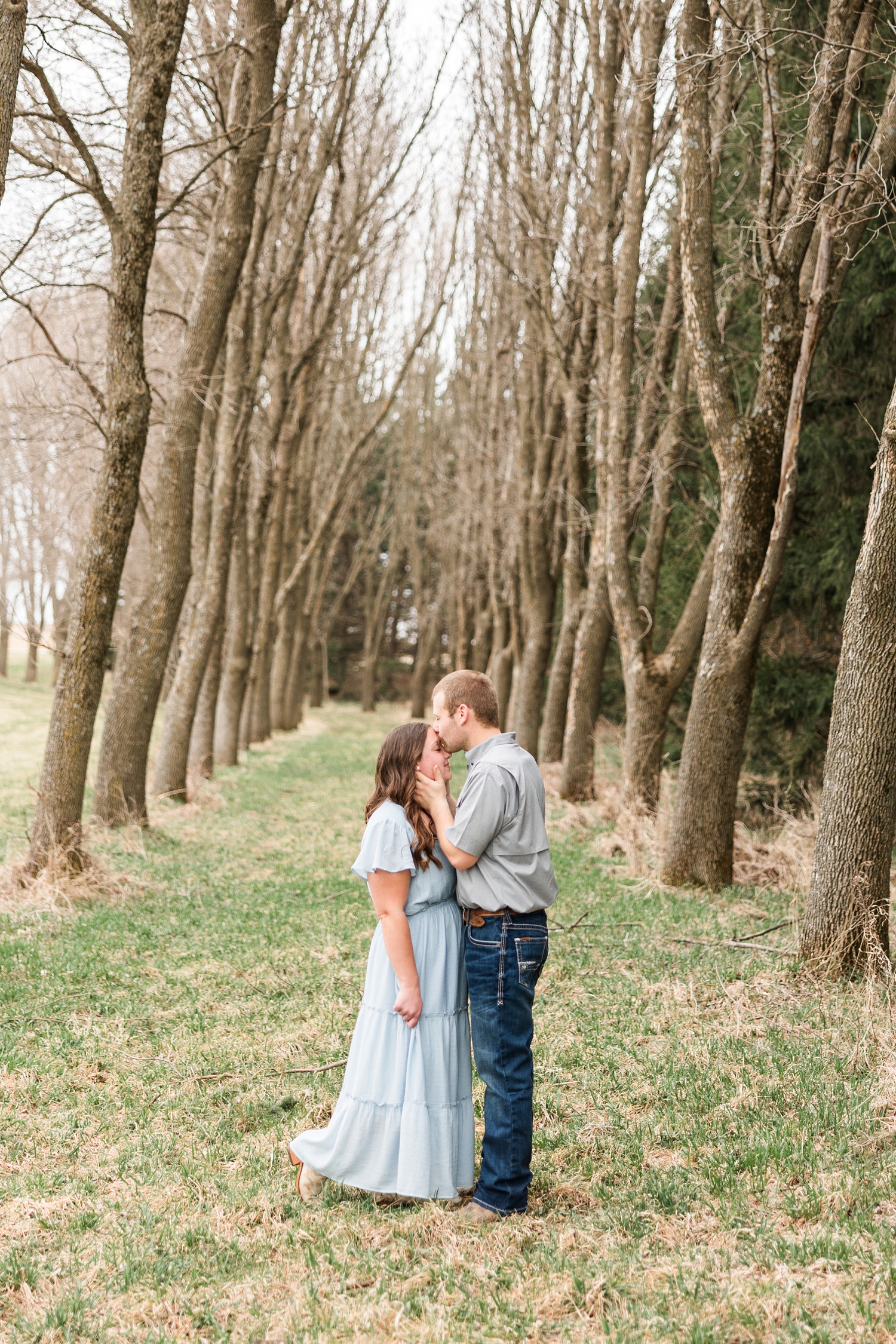 Ryan holds Cassie's cheeks and slowly pulls her in to kiss her forehead in the midst of a long tunnel of trees | CB Studio