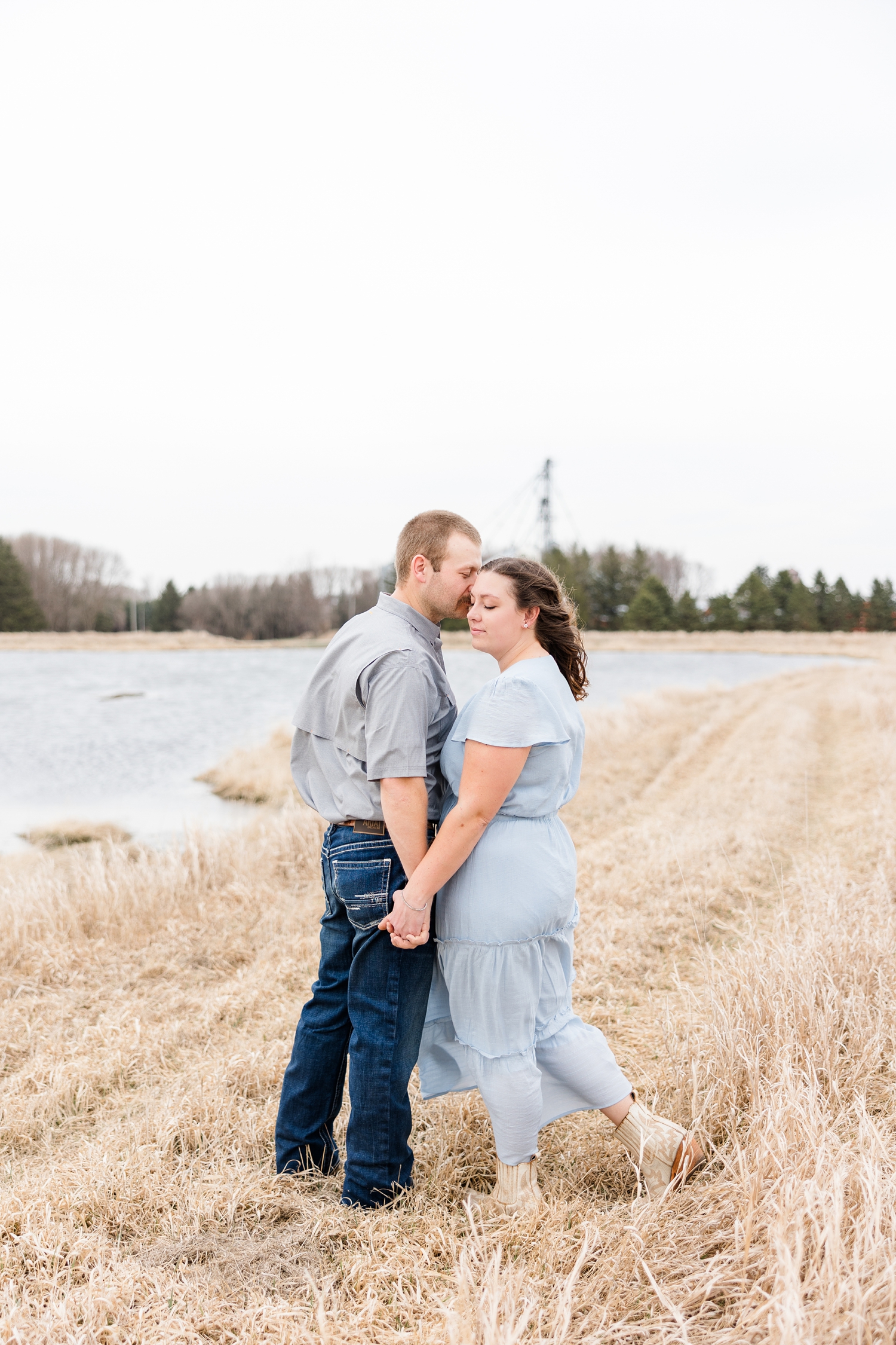 Ryan holds Cassie's hand and nuzzles her temple as she looks down over her shoulder with a country pond in the background | CB Studio
