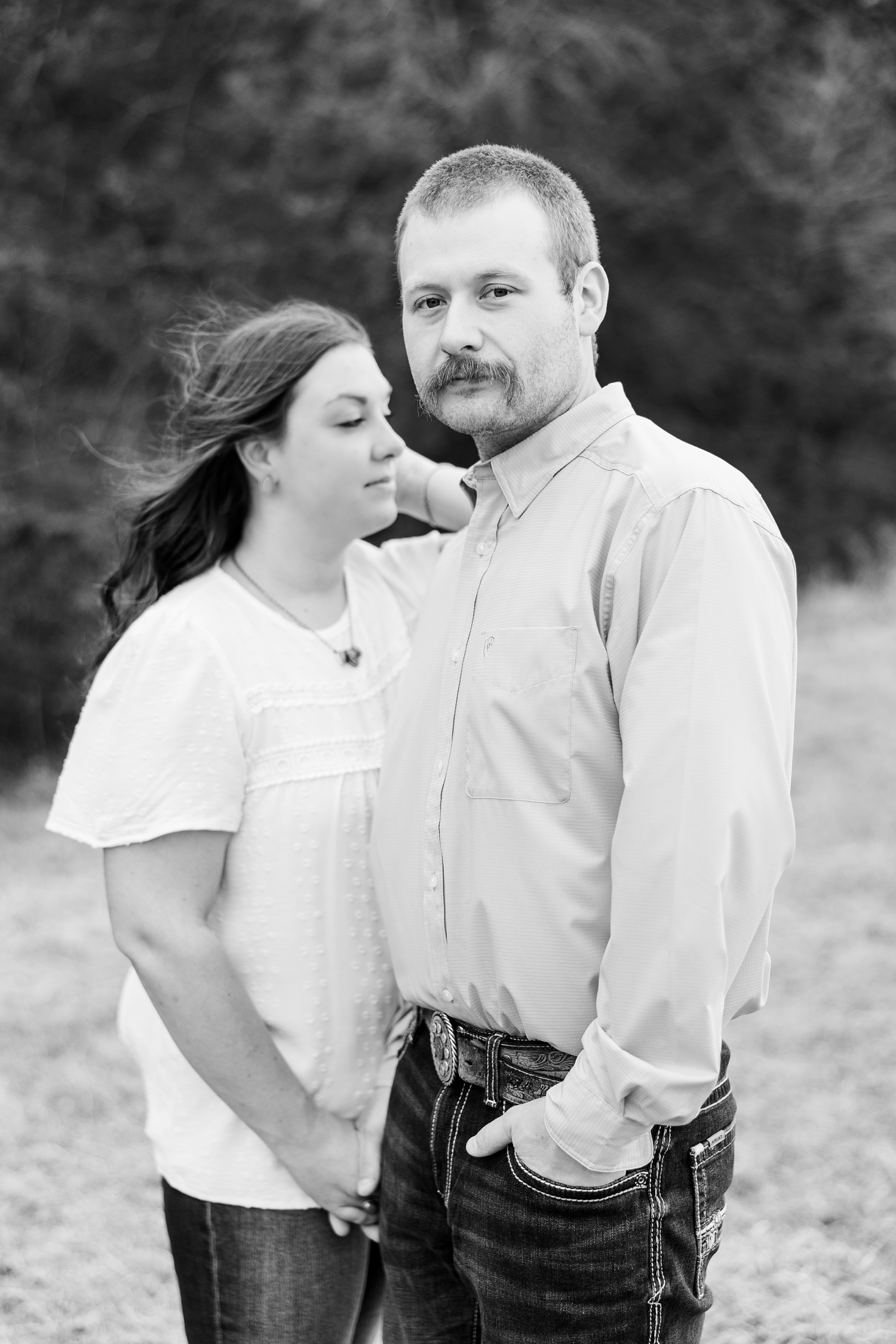 Ryan looks forward stoically while Cassie stands slightly in the background as she runs her fingers through her hair | CB Studio