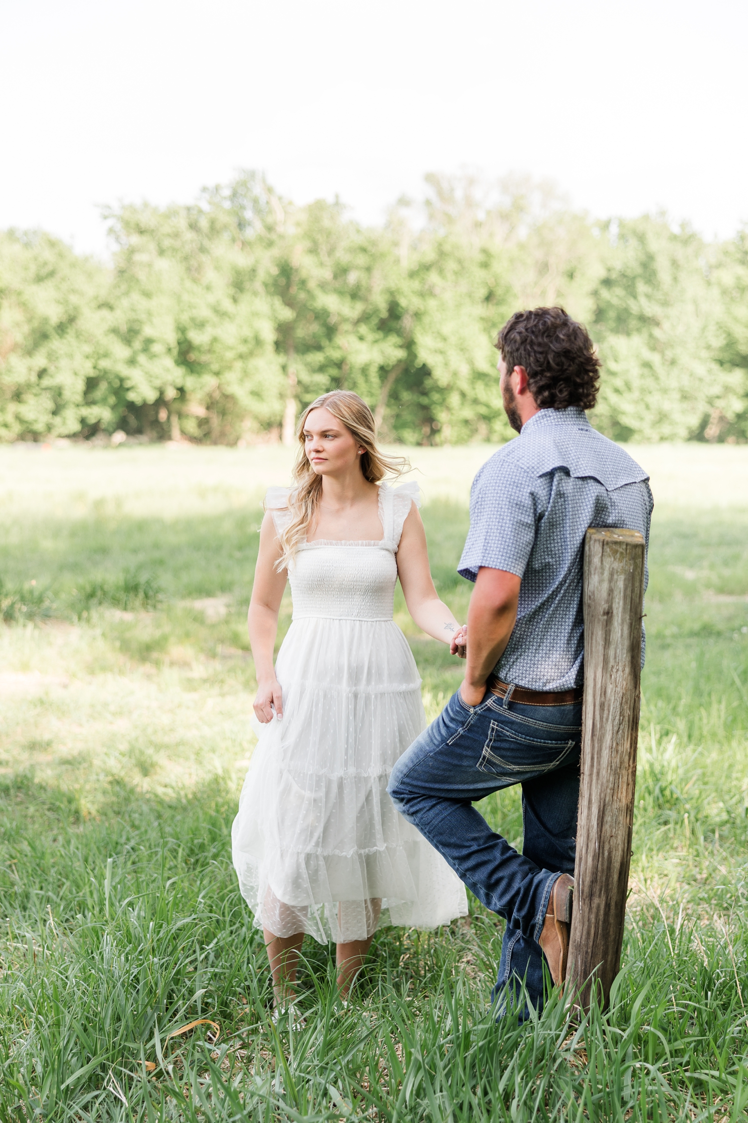 Dawson leans against an old fence post with his back to the camera, and Jade stands in front of him, holding his hand and looking to the left in the distance | CB Studio